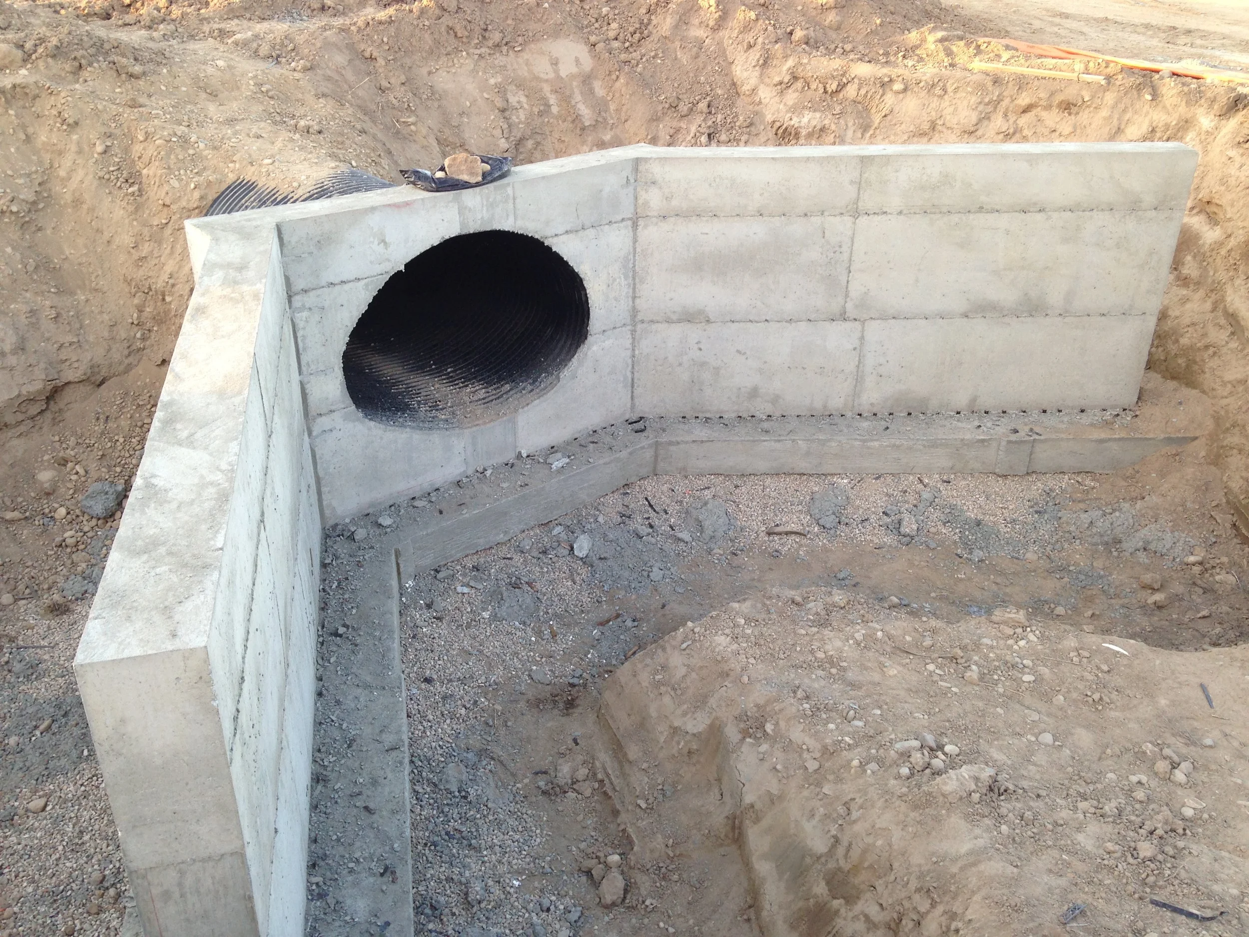 Concrete wall with a large circular pipe opening under construction on a dirt site.