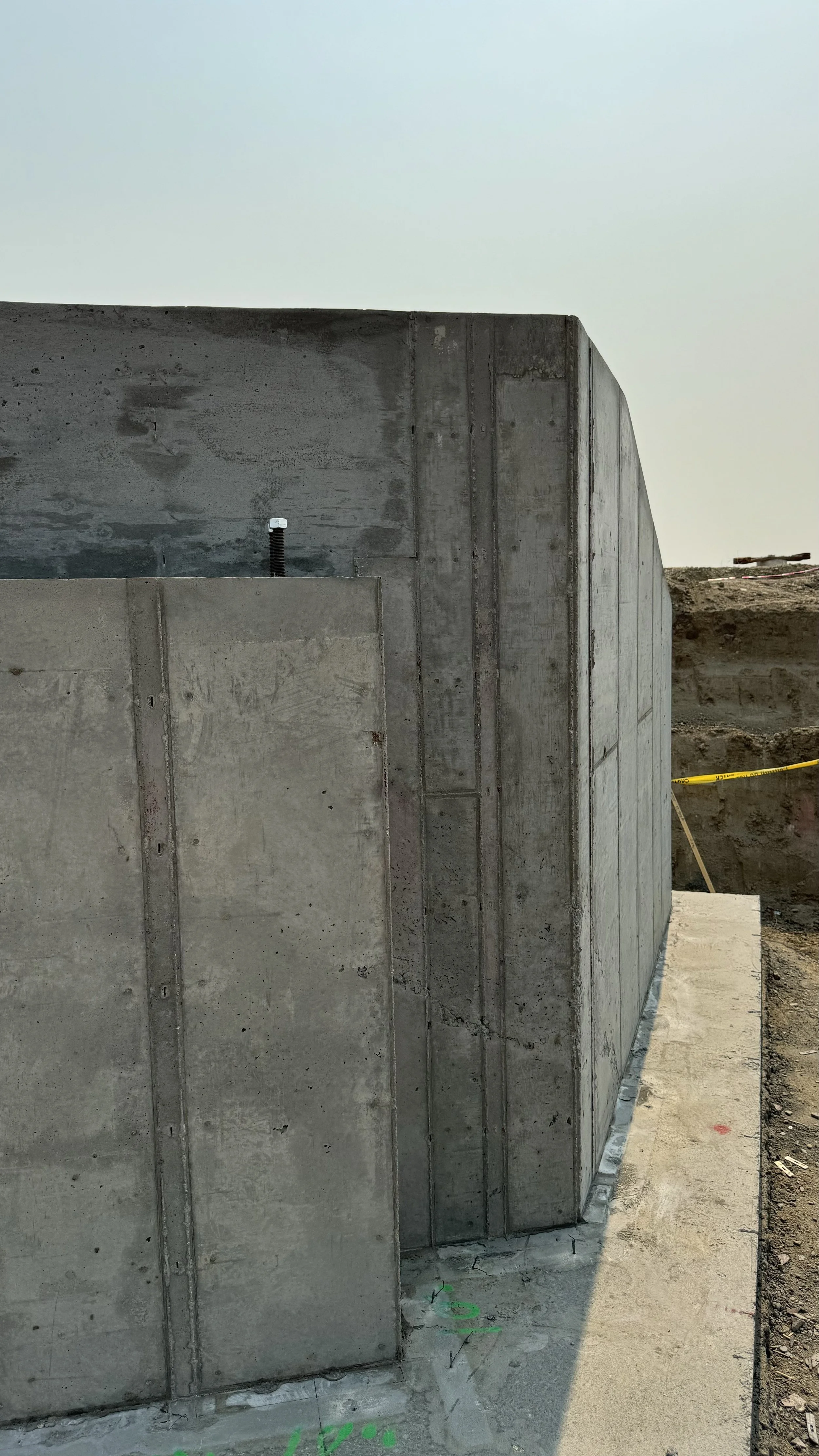 A new concrete wall at a construction site with construction markings on the ground and an electrical conduit protruding from the wall.