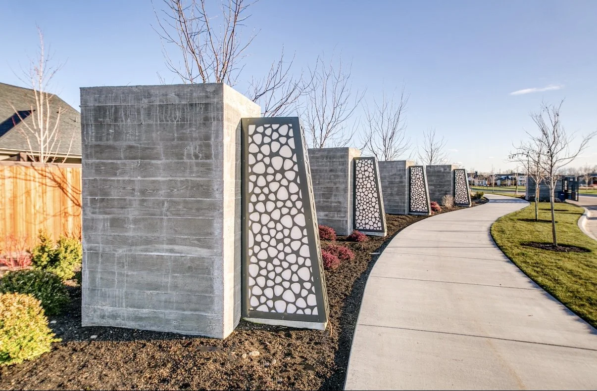 Concrete walls with decorative panels along a curved sidewalk in a landscaped area.