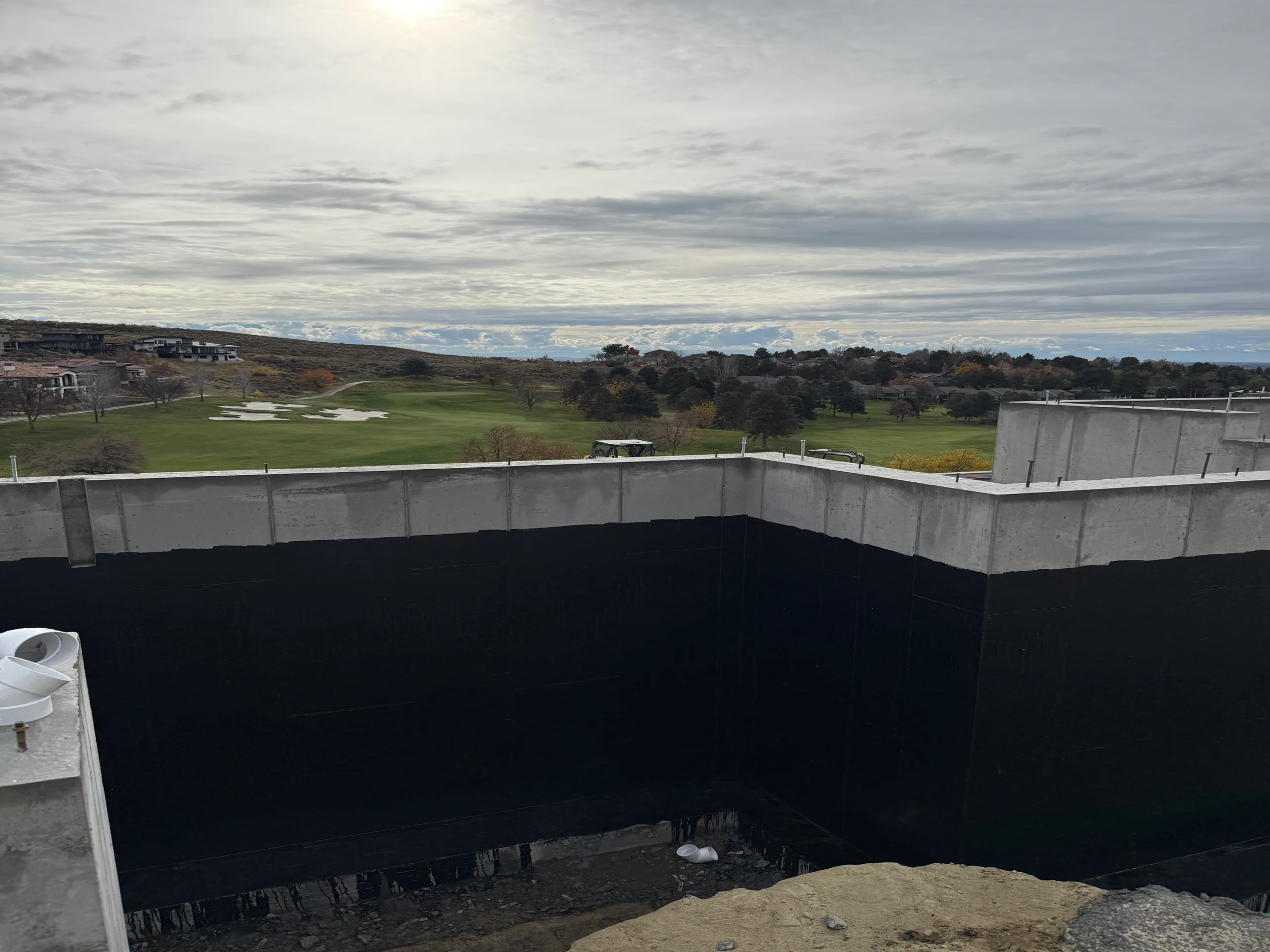 View from a construction site balcony showing a golf course with sand traps and trees, under a cloudy sky.