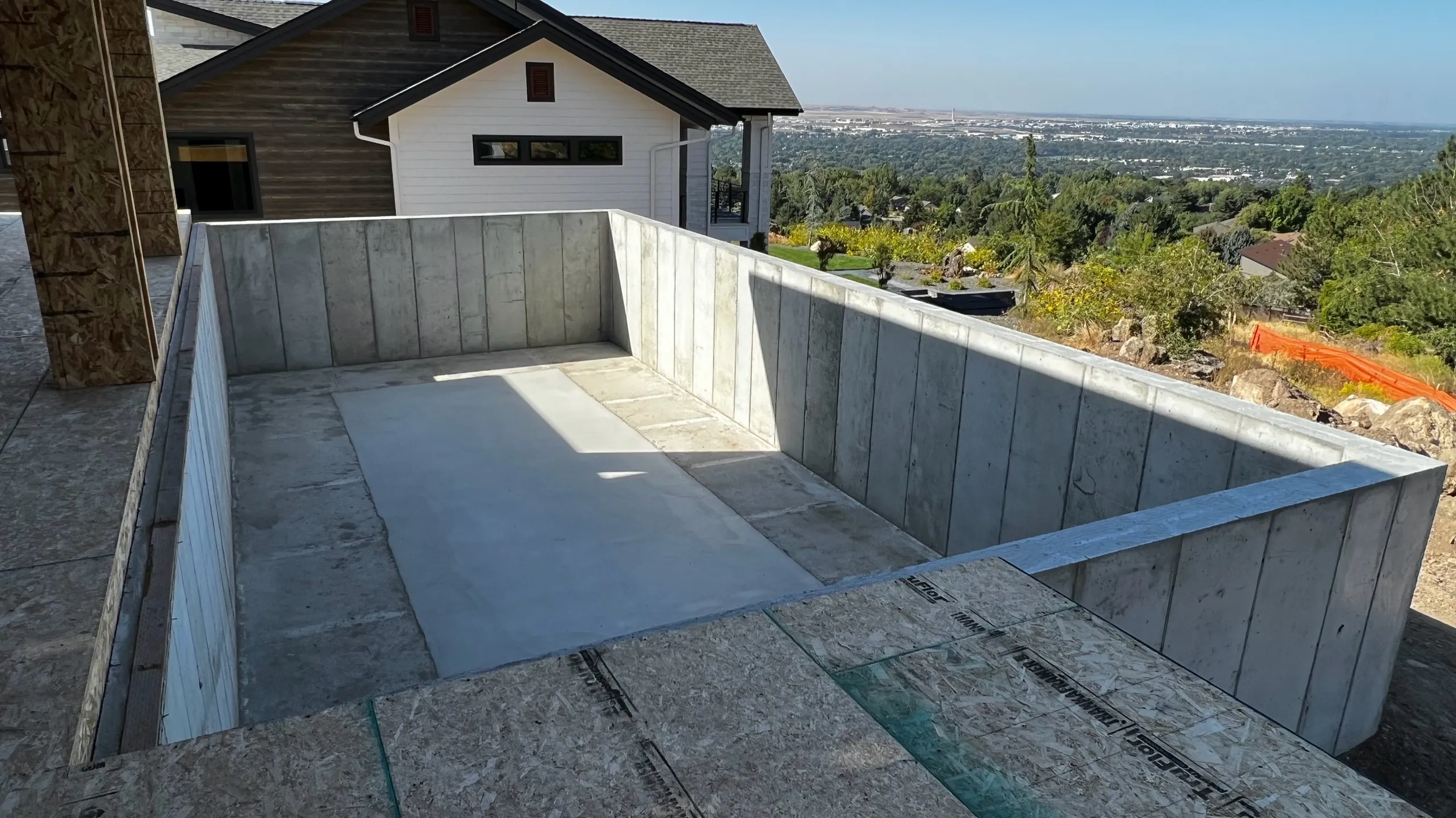 Concrete foundation and walls under construction on a building's balcony, with a view of a suburban landscape and trees in the distance.