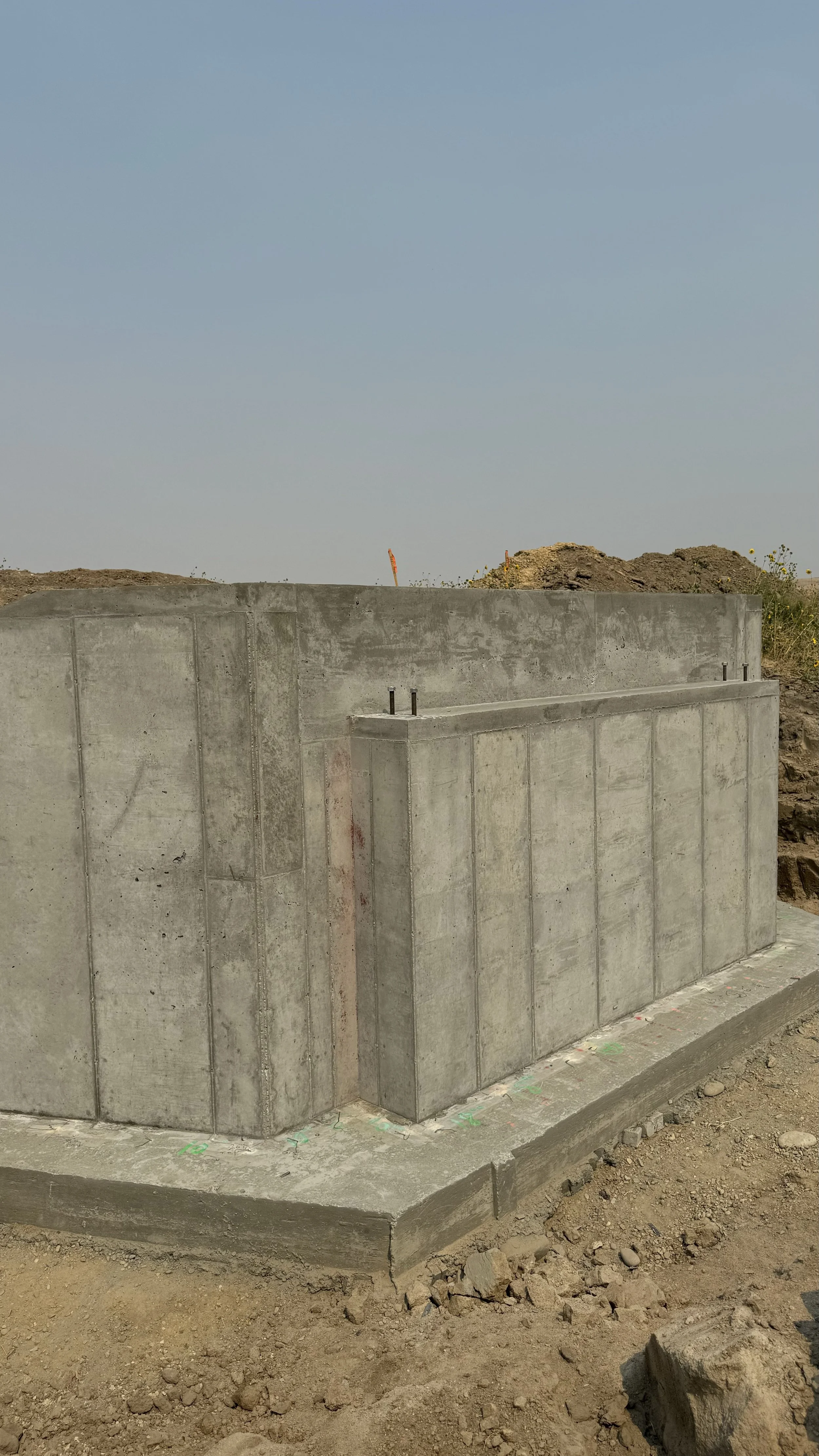 Concrete foundation walls and footing at a construction site, with a clear sky background.