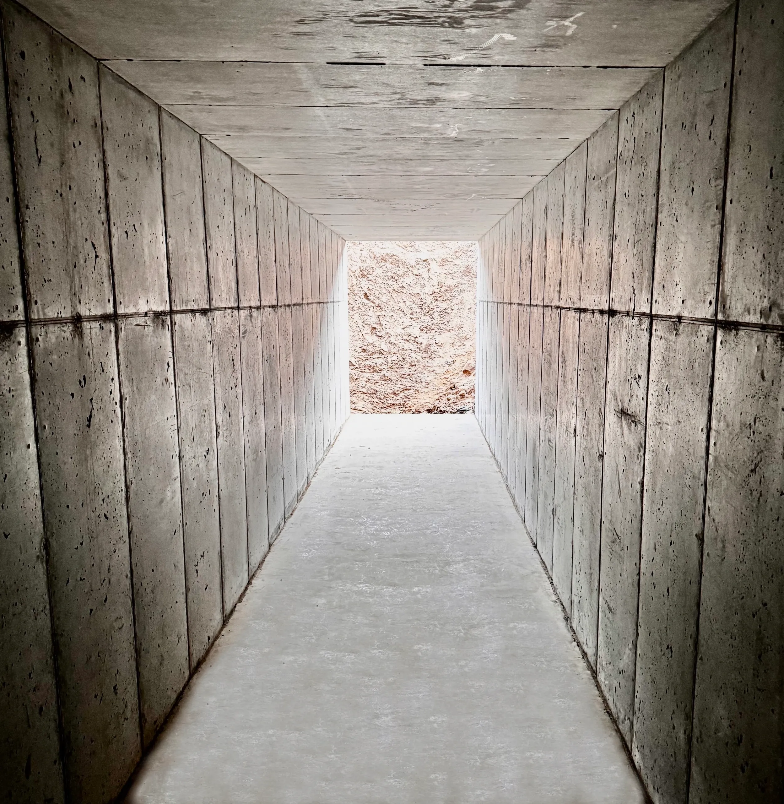 Concrete tunnel with rough-textured wall at the end, viewed from inside.