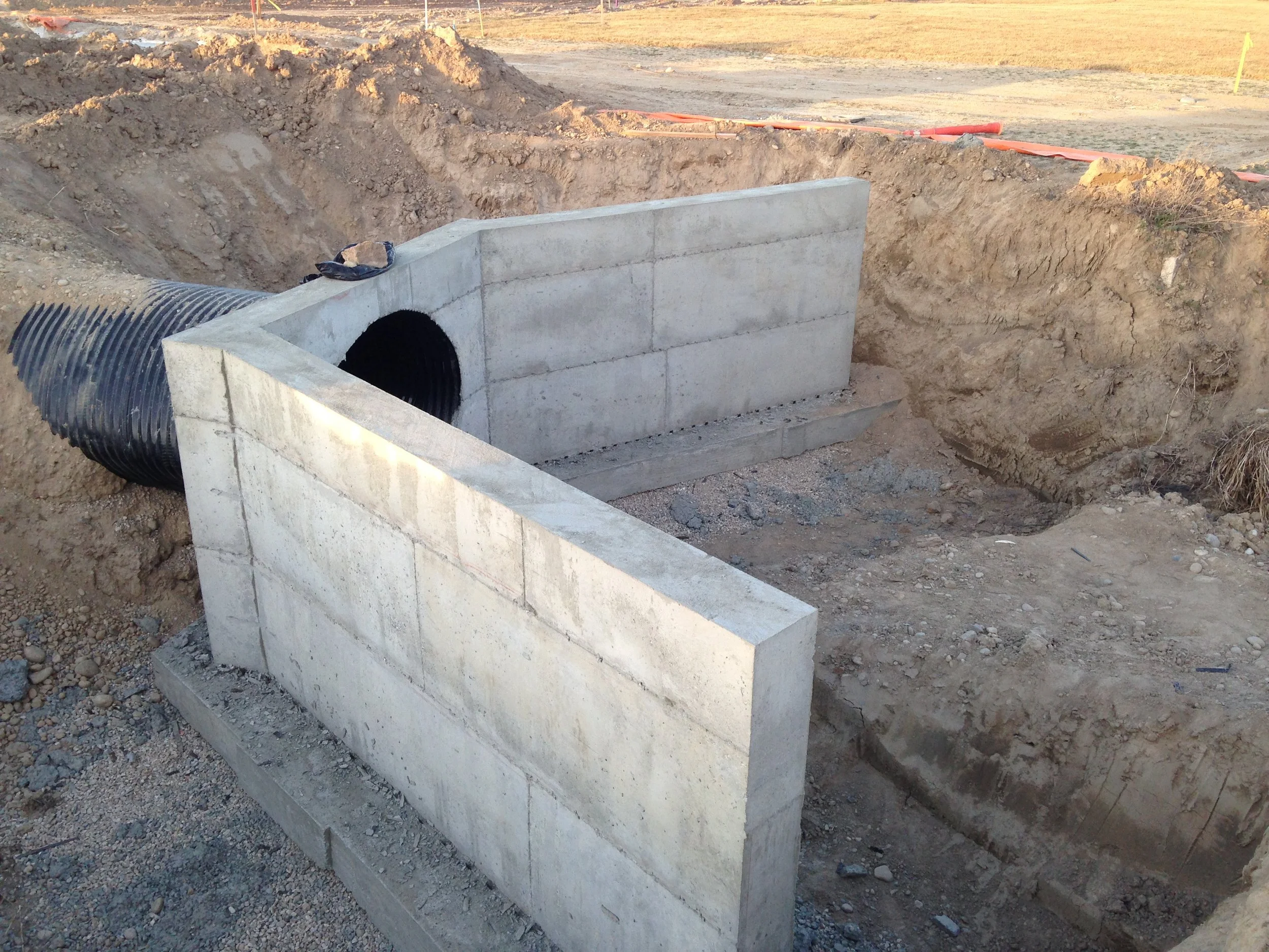 Construction site showing a concrete culvert with an attached black corrugated pipe, surrounded by dirt and excavation area.