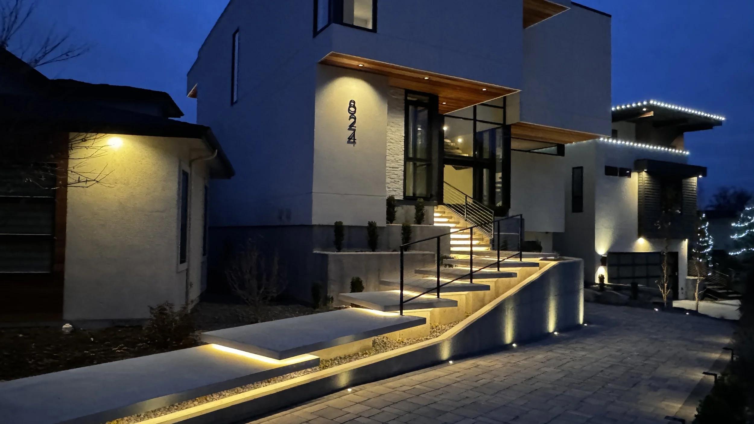 Modern house at night with illuminated stairs and exterior lighting, a house number 420 on the wall, and a driveway.