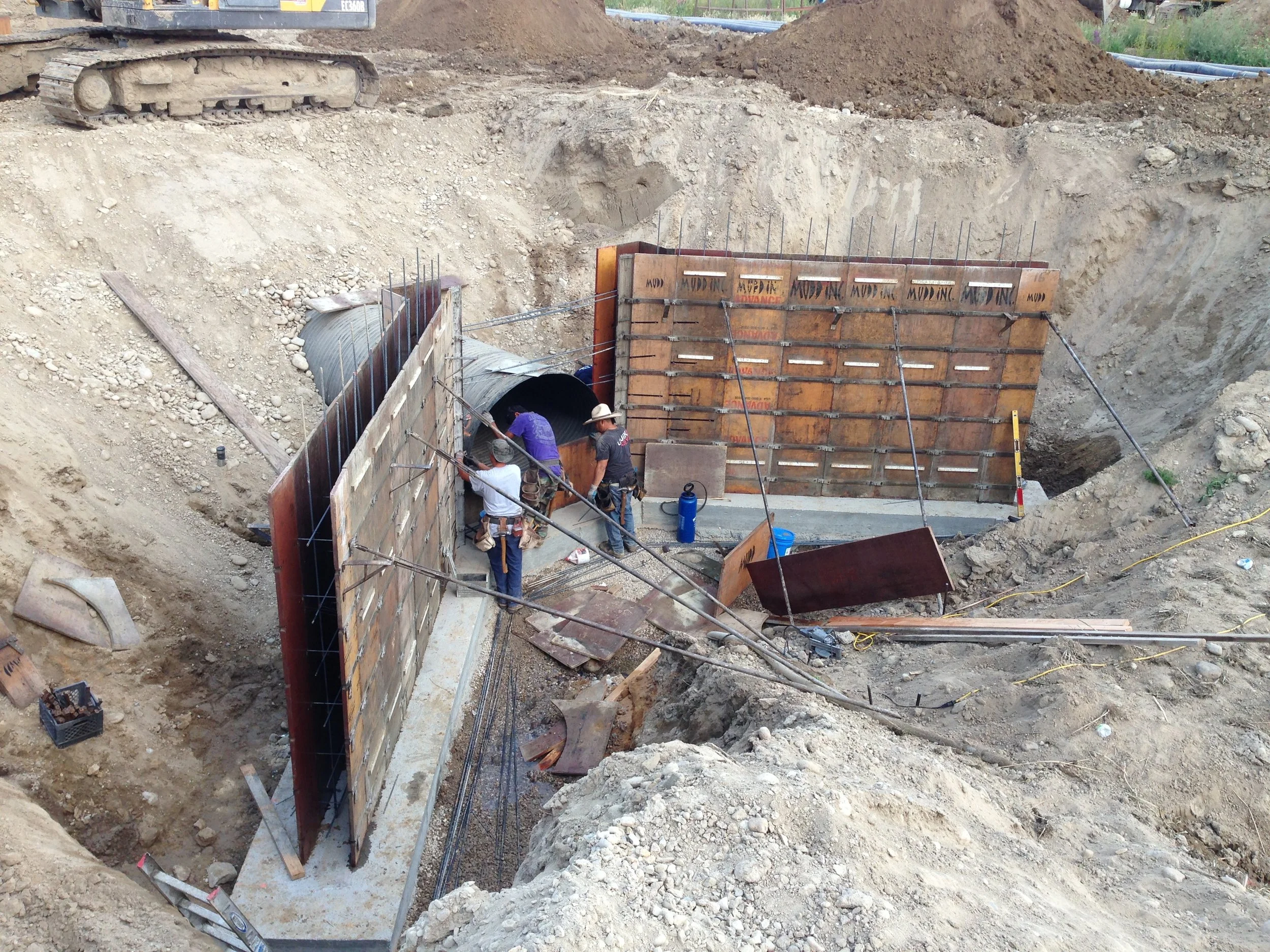 Construction workers installing a tunnel in the ground with metal and wooden support structures and construction equipment around.