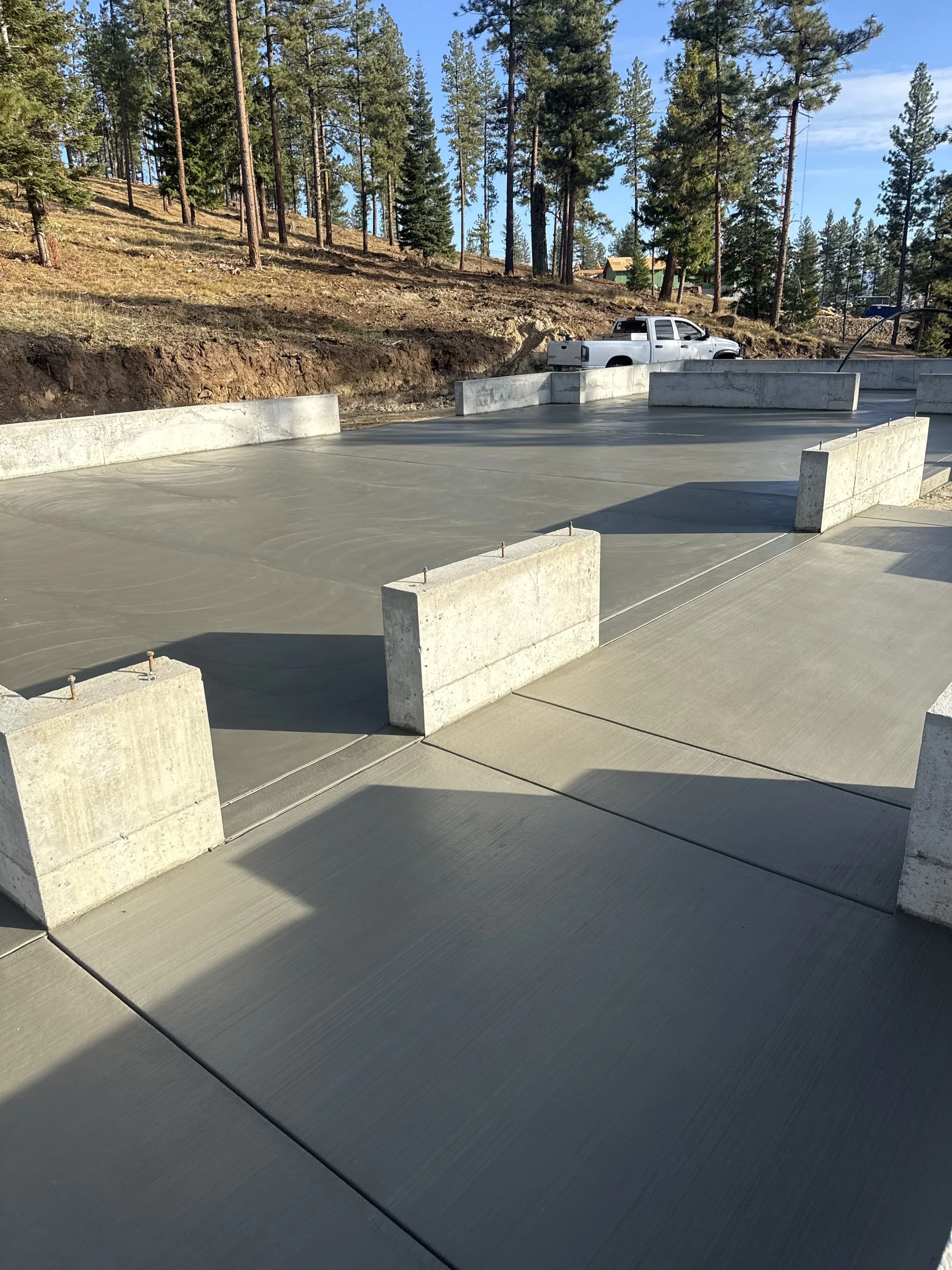 Concrete foundation and pavement, with concrete barriers, surrounded by a forested hillside and parked truck in the background.
