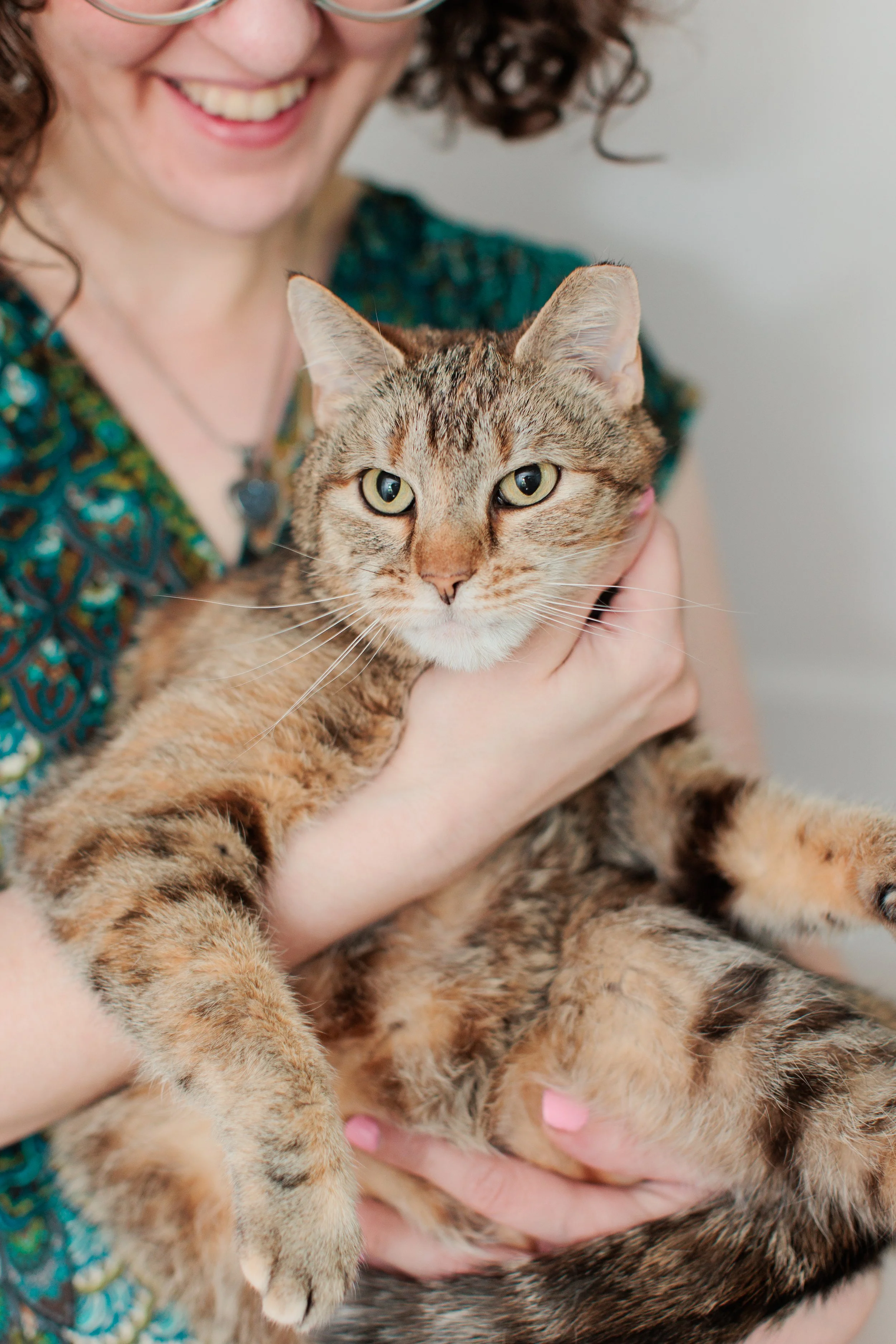 Chelsea Turner smiles while holding a tabby cat in her arms. The cat looks toward the camera with its front paws resting comfortably over her arm.