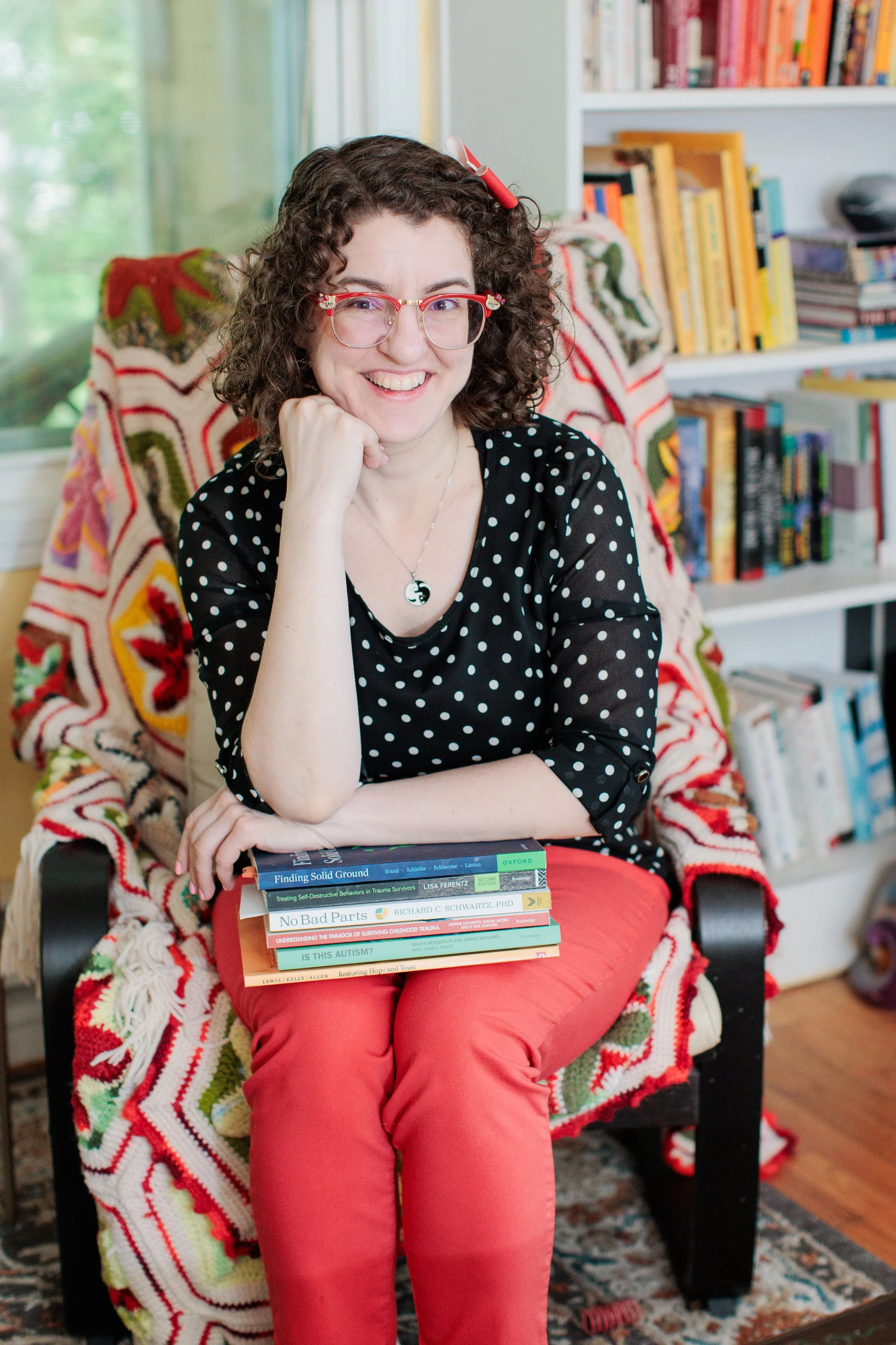 Chelsea Turner, founder of Chelsea Turner Therapy, smiles in her office while holding books on trauma, dissociation, autism, and neurodiversity. She provides trauma-informed, psychodynamic therapy for adults throughout Maryland and Washington, DC.