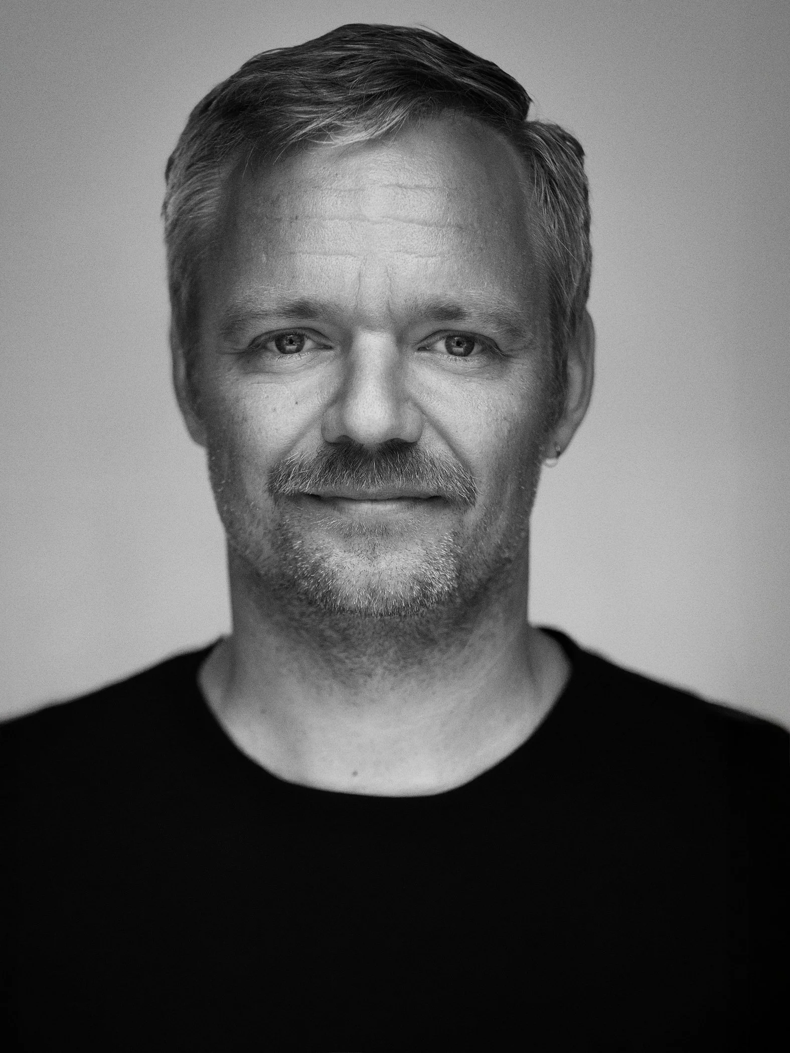 Black and white portrait of a middle-aged man with light hair, a beard, and a slight smile, wearing a black shirt.