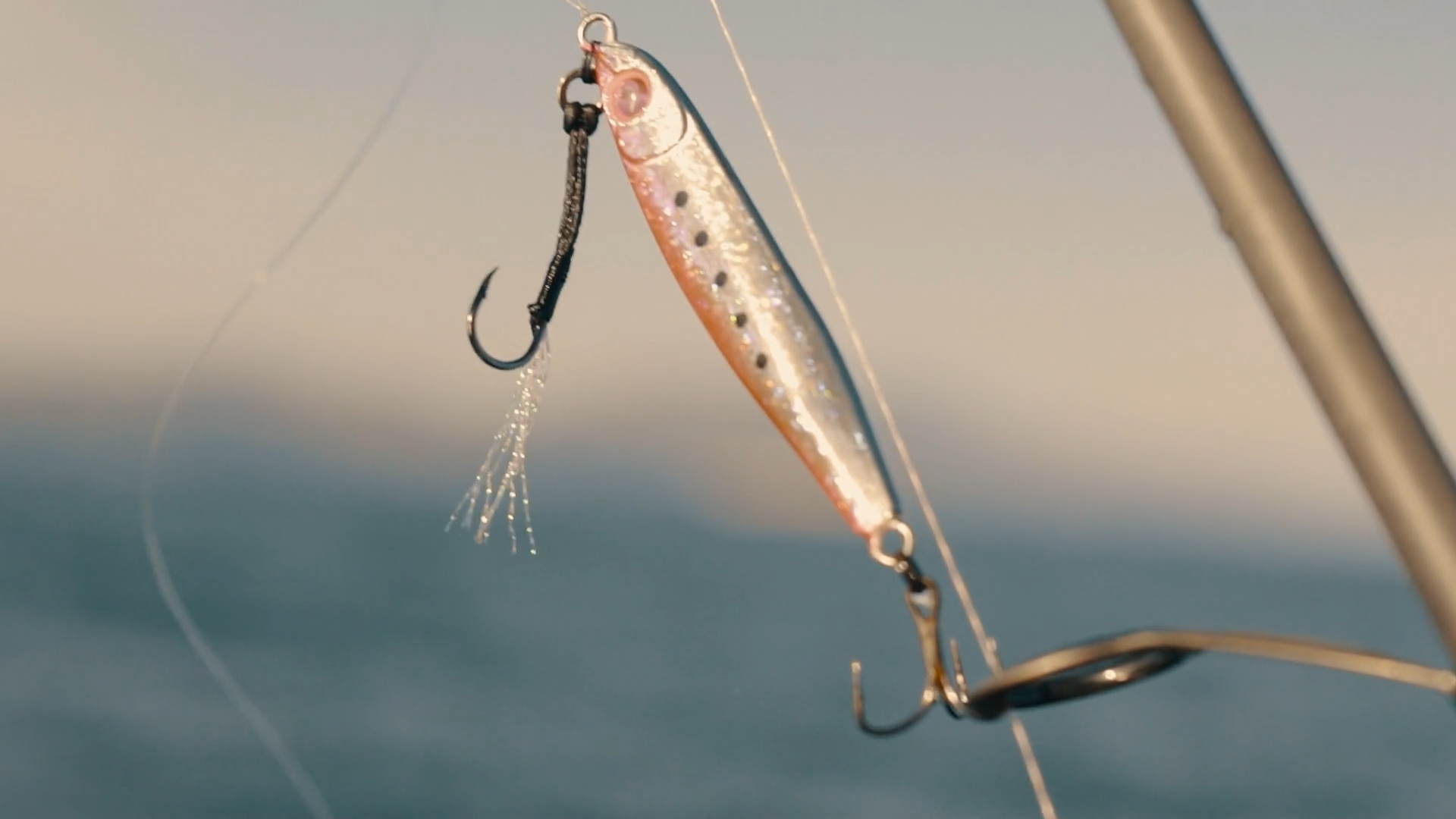 Close-up of a fishing lure with two treble hooks, hanging from a fishing rod over water.