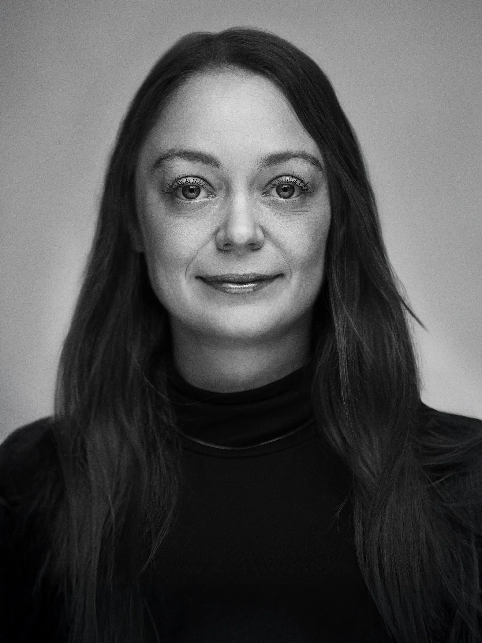 Black and white portrait of a woman with long dark hair, wearing a turtleneck shirt, looking directly at the camera with a slight smile.