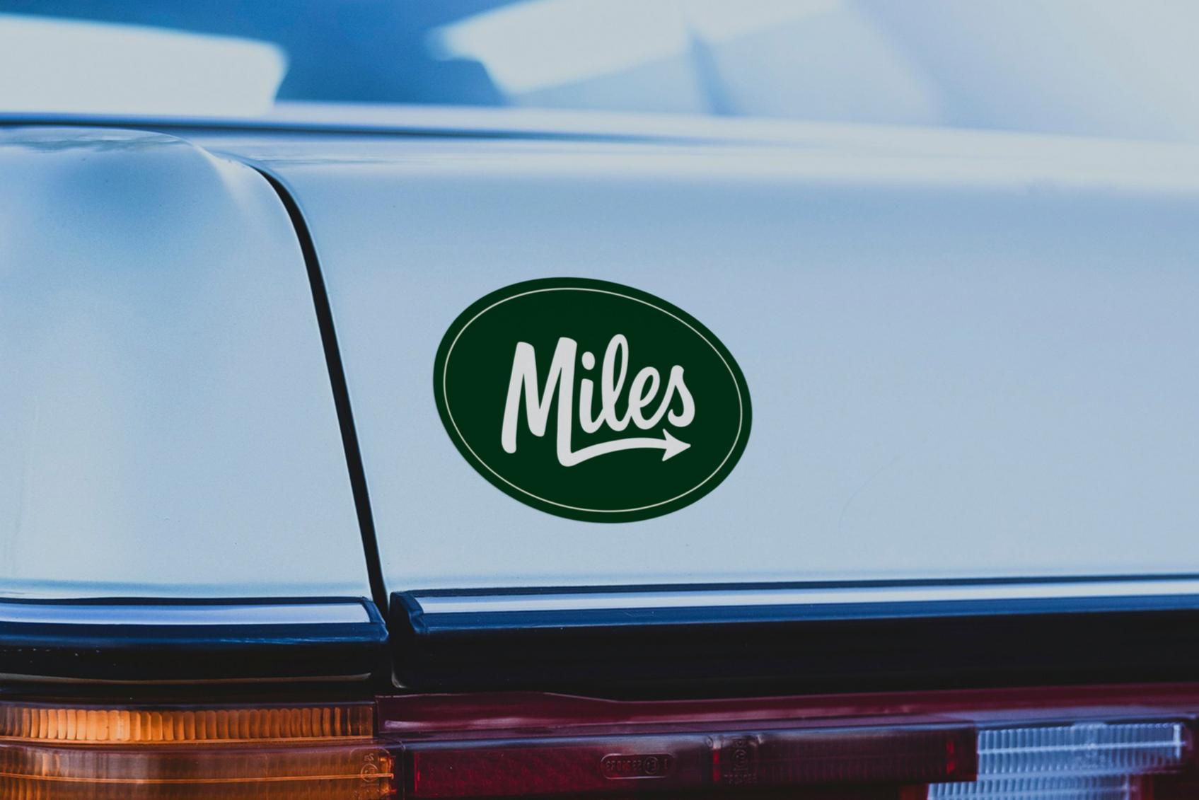 A close-up of a classic car's rear with a green and white 'Miles' bumper sticker.