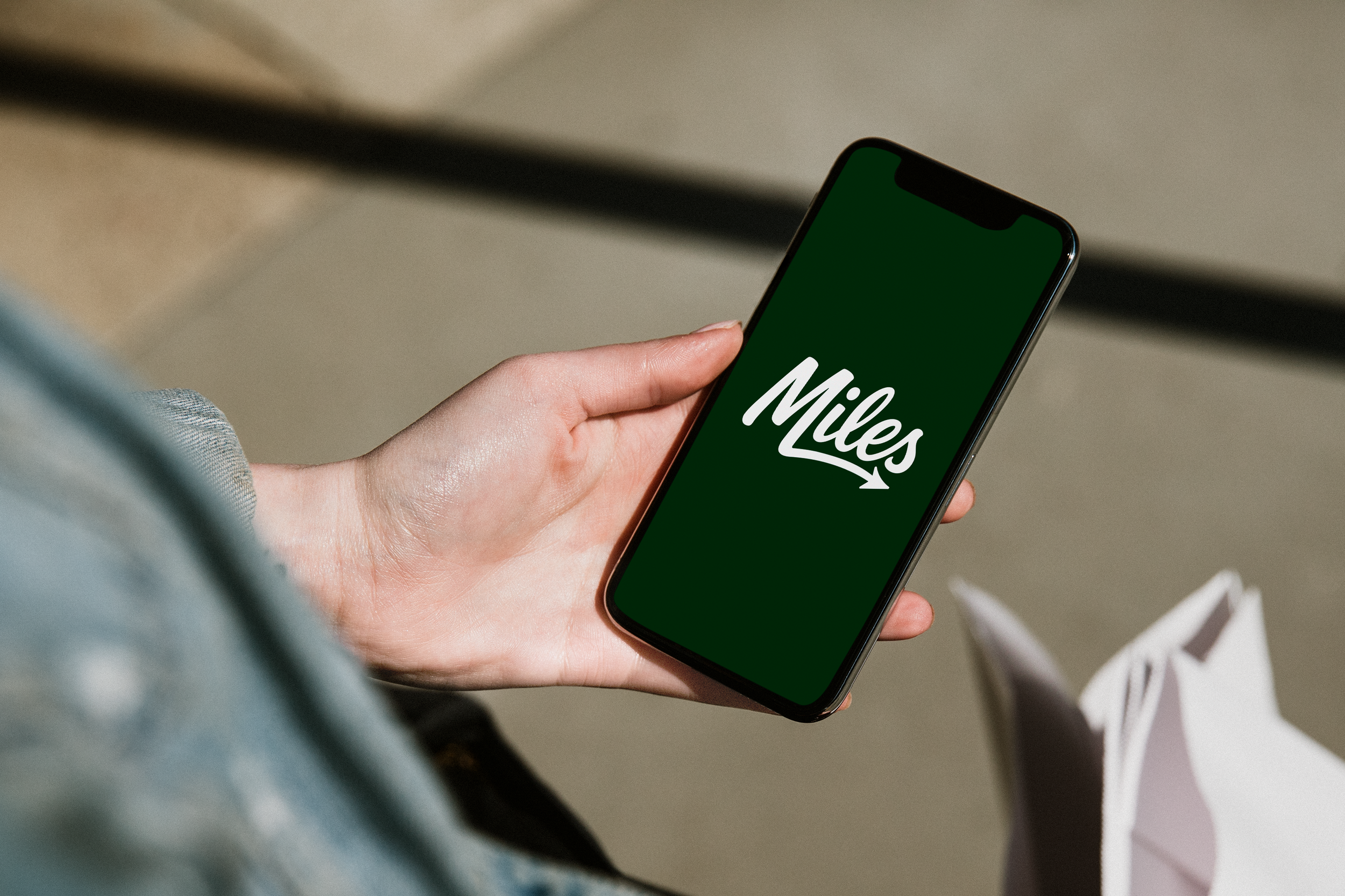Close-up of a hand holding a smartphone with the Miles app logo on the screen.