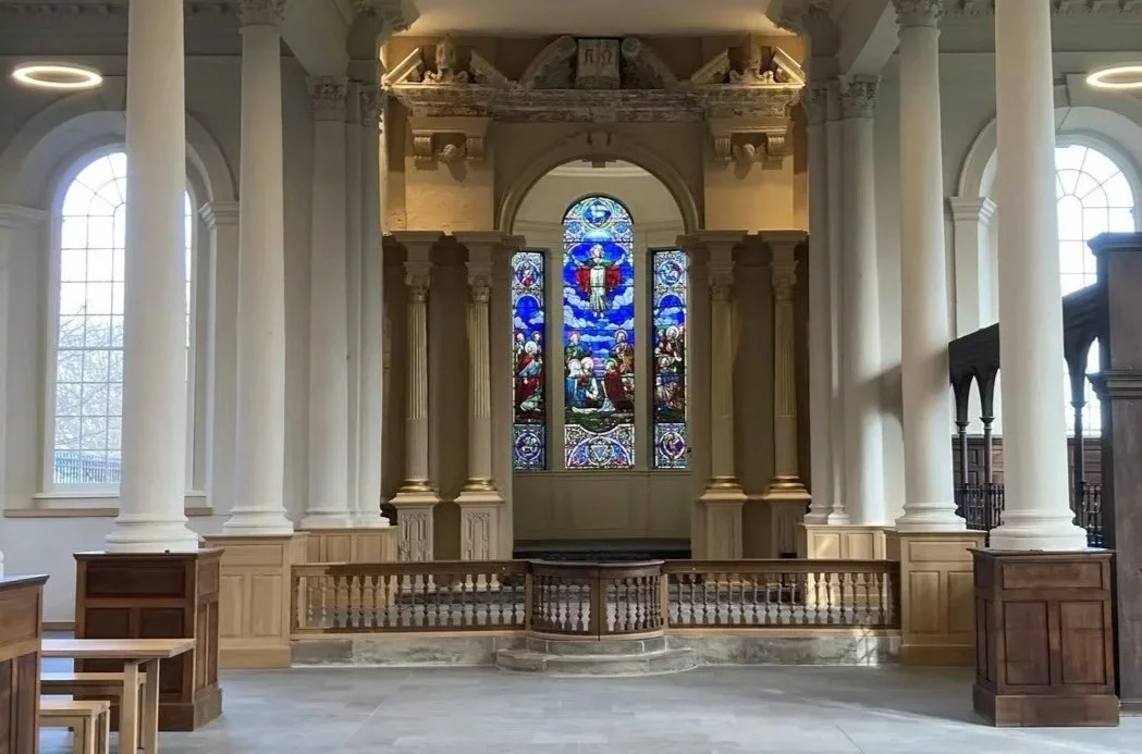 17 Nineteen events space, Sunderland. View of a church altar with stained glass window, surrounded by white columns and wooden railings, inside a historic church building. which is now used as a community events and arts space