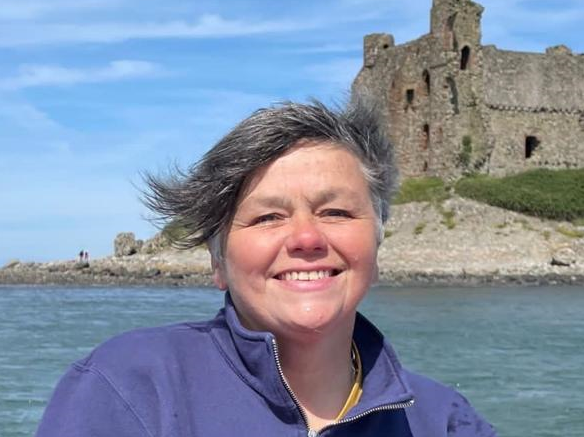 Karen Houghton on a boat over to Piel Island, Cumbria. The sky is blue and there are people standing on the headland looking out to sea.