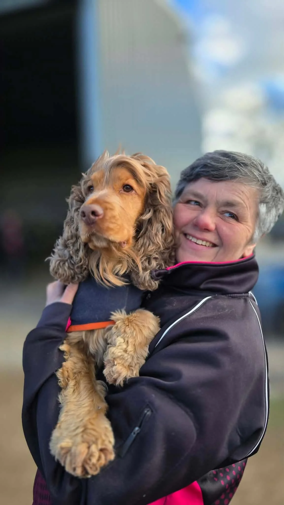 A smiling woman holding a cocker spaniel puppy outdoors.