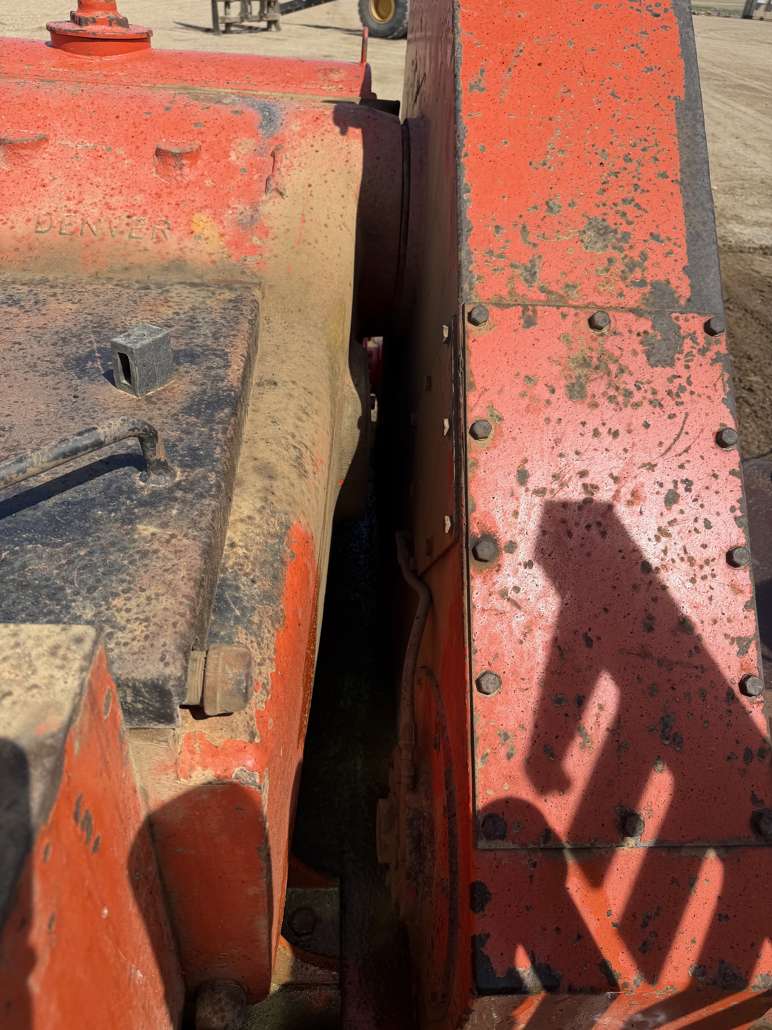 Close-up of a weathered orange construction vehicle or machinery part with bolts and rust, on a dirt ground.