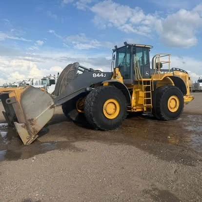 A yellow front loader with large black tires and a gray bucket attachment on a dirt surface under a partly cloudy sky.