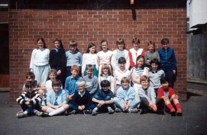 Group of children posing for a class photo outside against a brick wall.