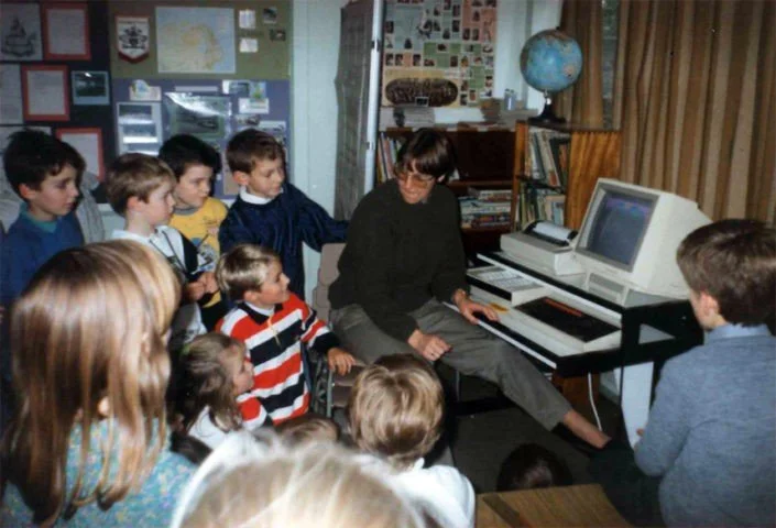 A male teacher or instructor showing a group of children a computer and keyboard in a classroom.