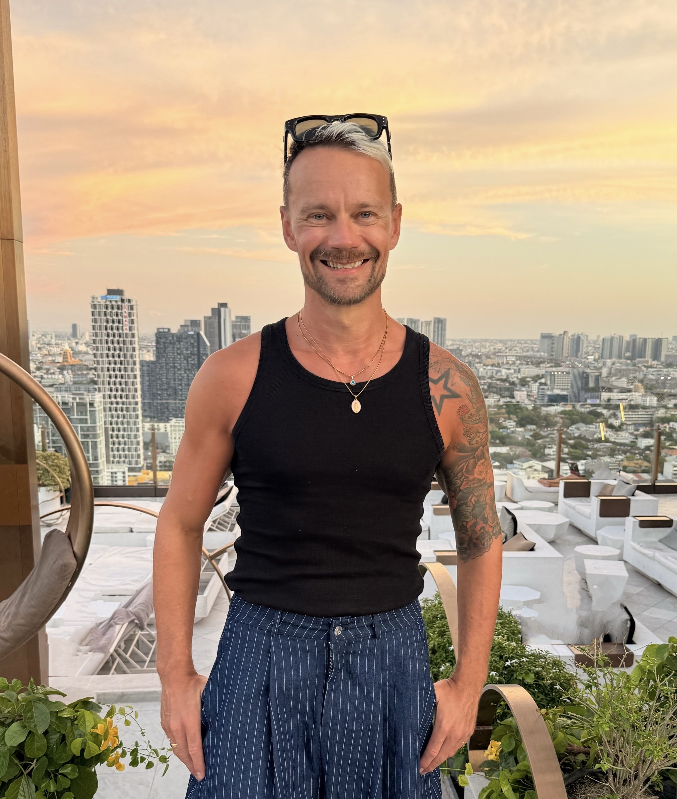 A woman with long brown hair seated on a chair in front of a beige background, with a photography backdrop stand visible behind her.