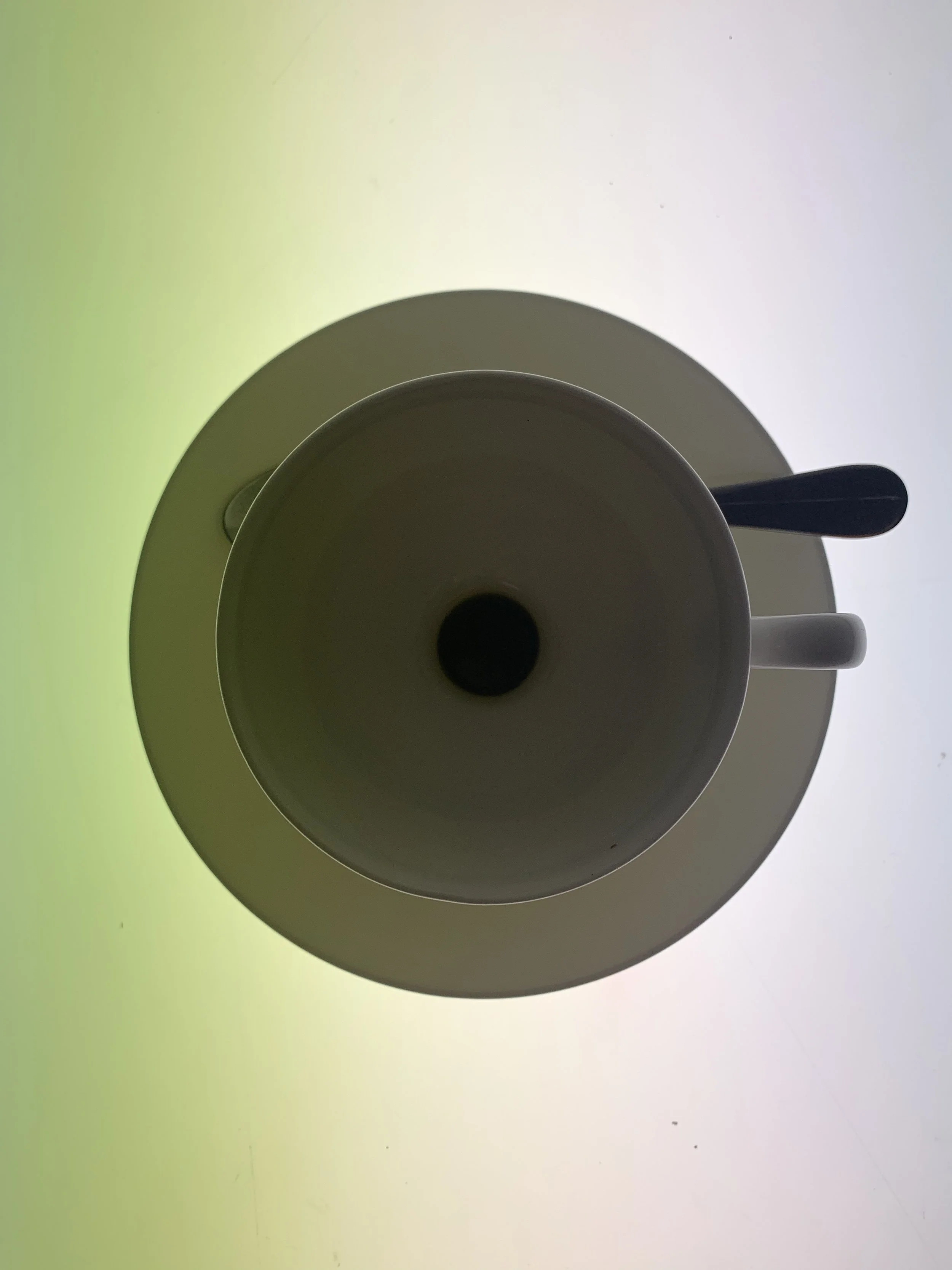 The remains of tea and conversation, we see an overhead view of a teacup placed on a saucer, with a spoon inside the cup, on a luminous gradient background.