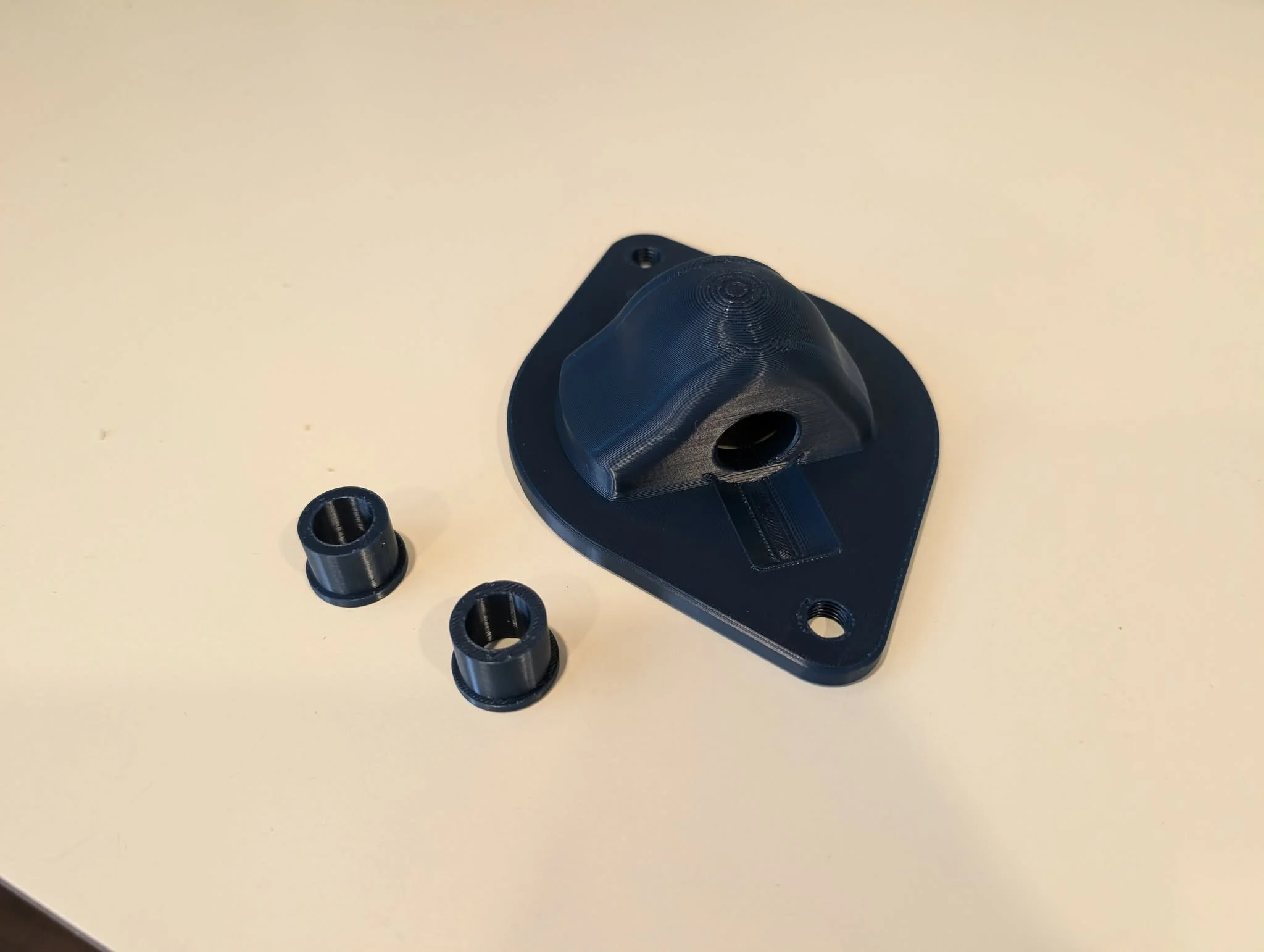 A 3D-printed black plastic piece with multiple holes on a cream-colored surface, with several smaller black 3D-printed parts around it.