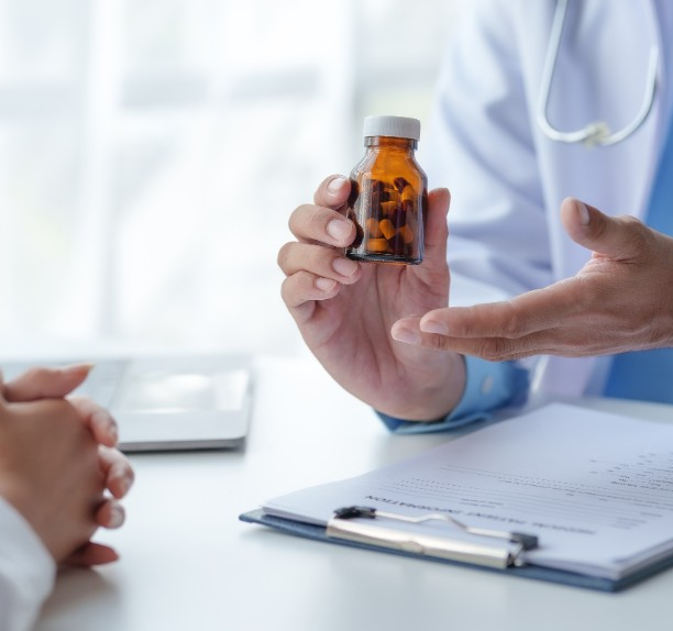 Doctor holding a bottle of pills during consultation with a patient in a bright office.  This is a reflection of our medication management services and also that we work with our patients when making medication decisions.