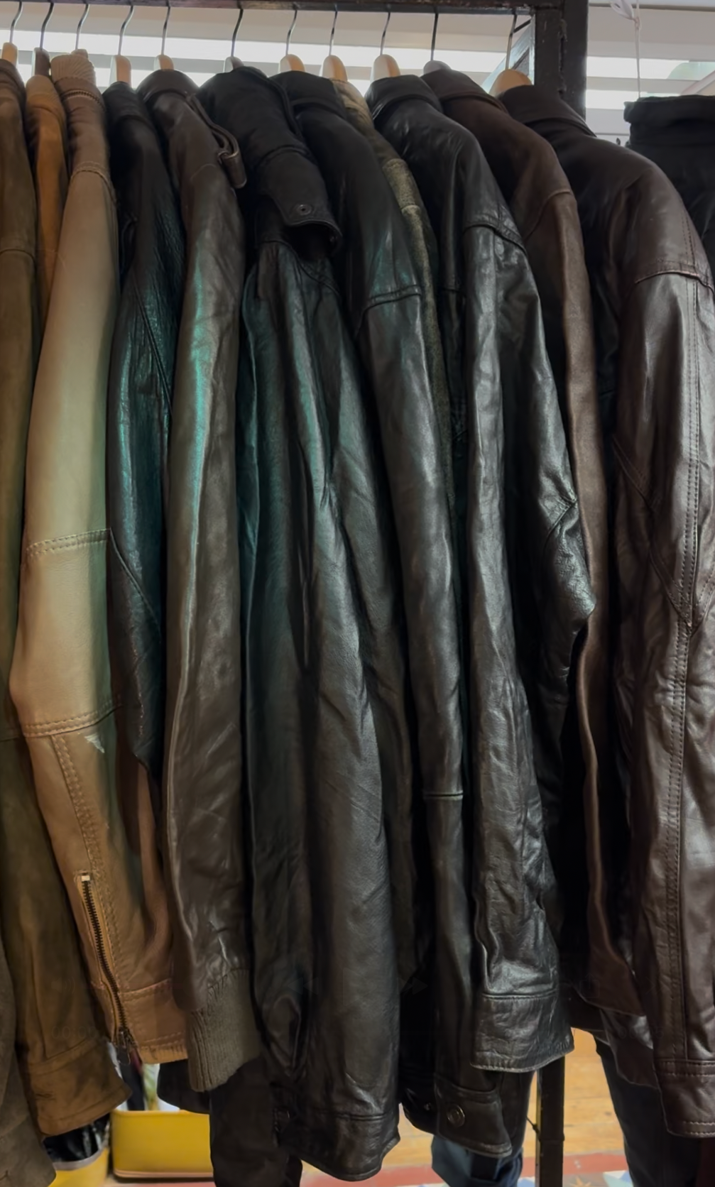 A row of leather and fabric jackets hanging on a clothing rack inside a store.