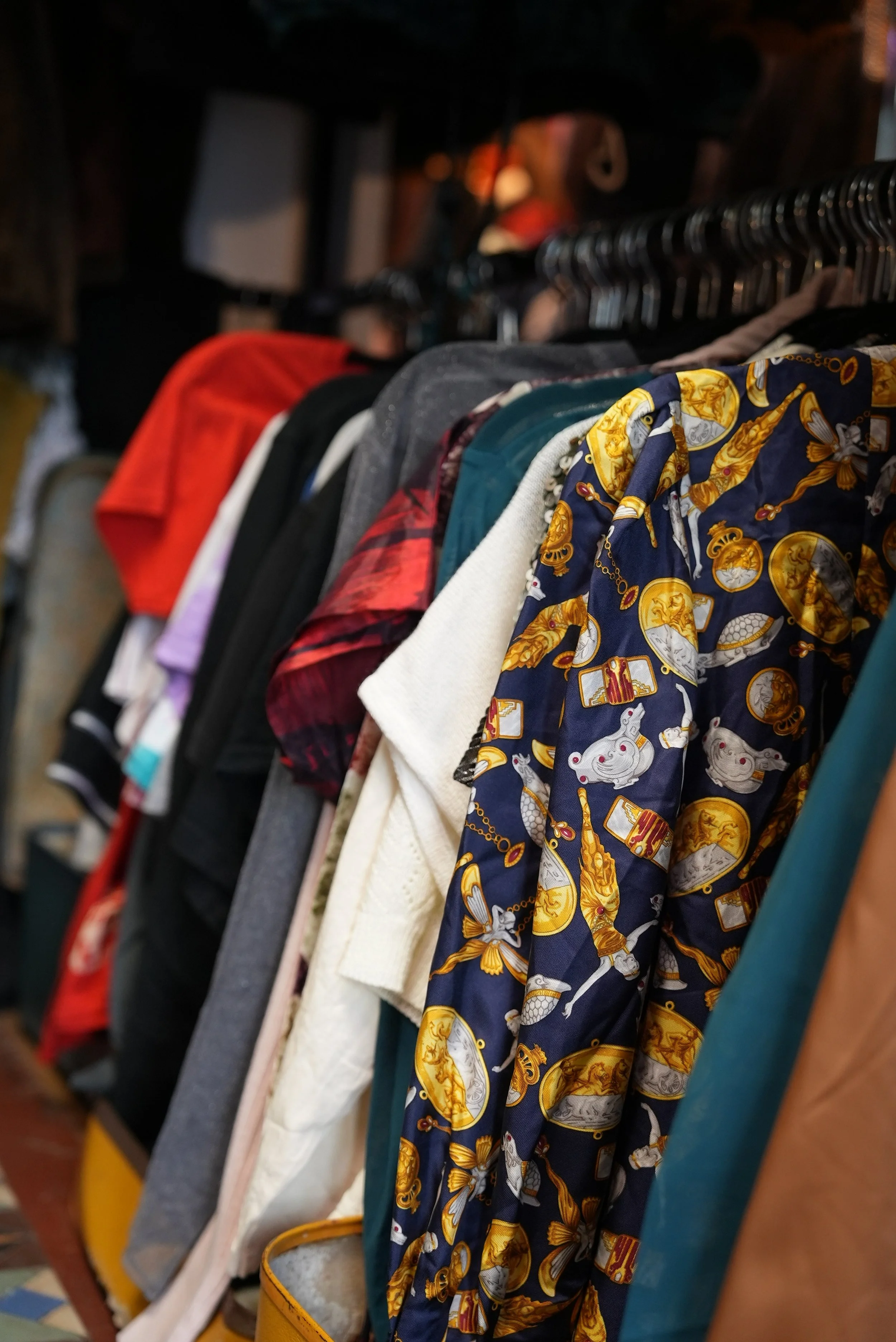 Clothing rack with colorful jackets and shirts in an indoor thrift store.