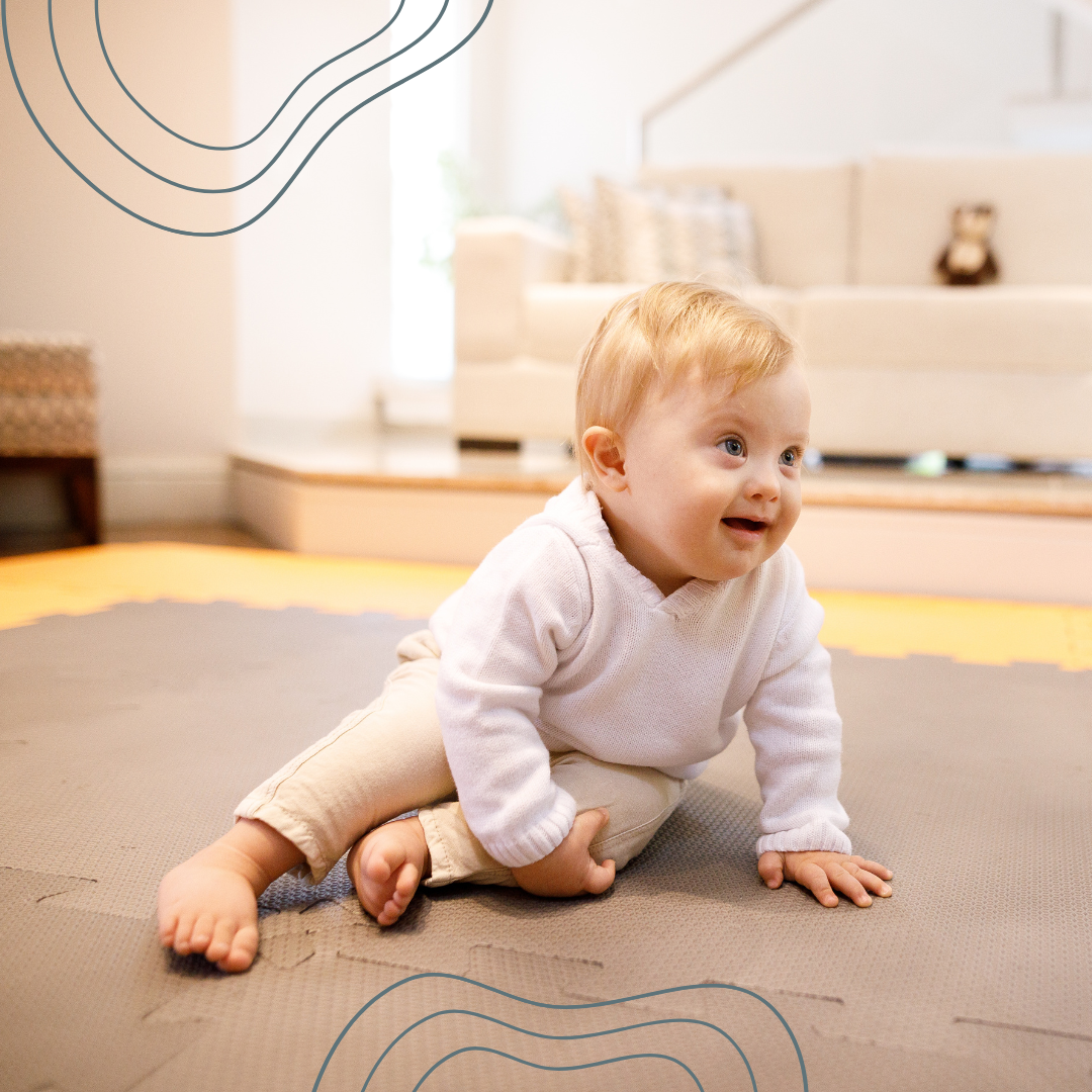 An infant crawling on a foam mat in a bright living room, with a sofa and decorative pillows in the background.