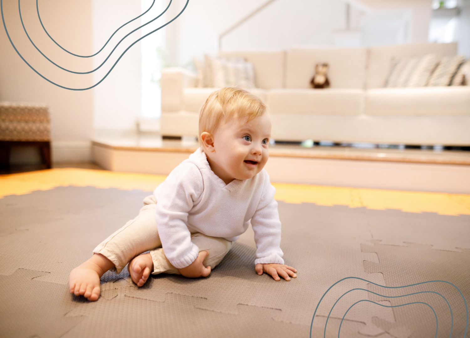 An infant crawling on a foam mat in a bright living room, with a sofa and decorative pillows in the background.
