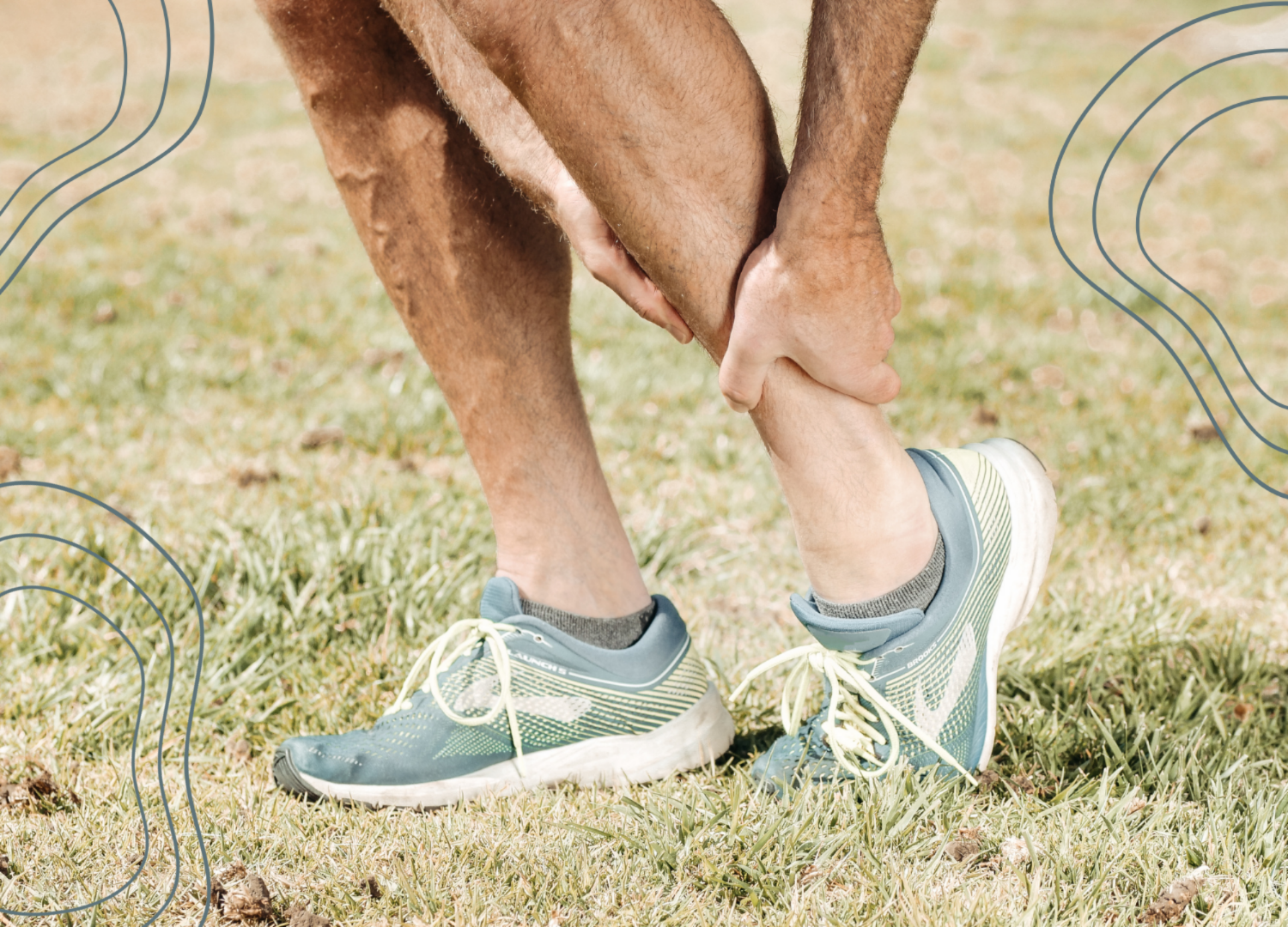 Person wearing blue athletic shoes, gray socks, and gray shorts, touching their leg while outdoors on grass.