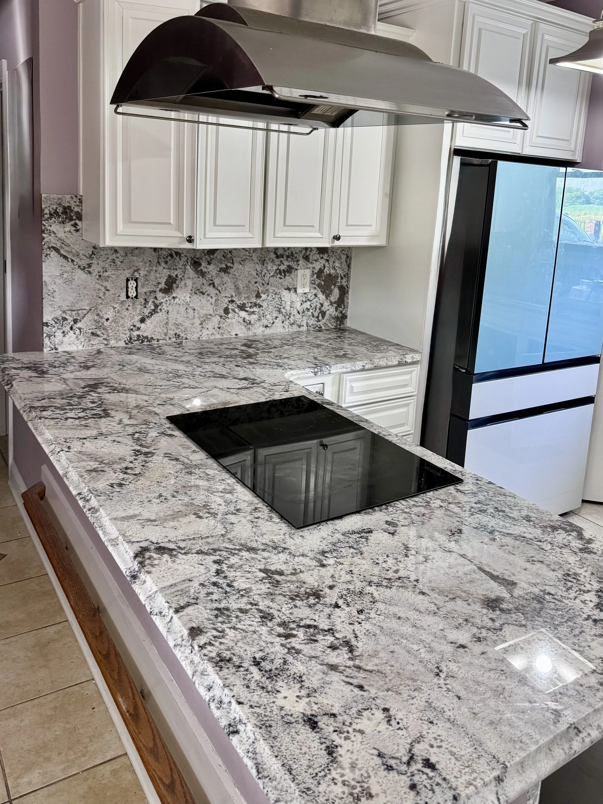 Kitchen with granite countertops, white cabinets, a black cooktop, a range hood, and a large black and white refrigerator.