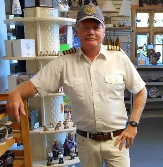 A man in military uniform with a captain's hat and shoulder epaulets standing inside a store with shelves of decorative items and figurines.