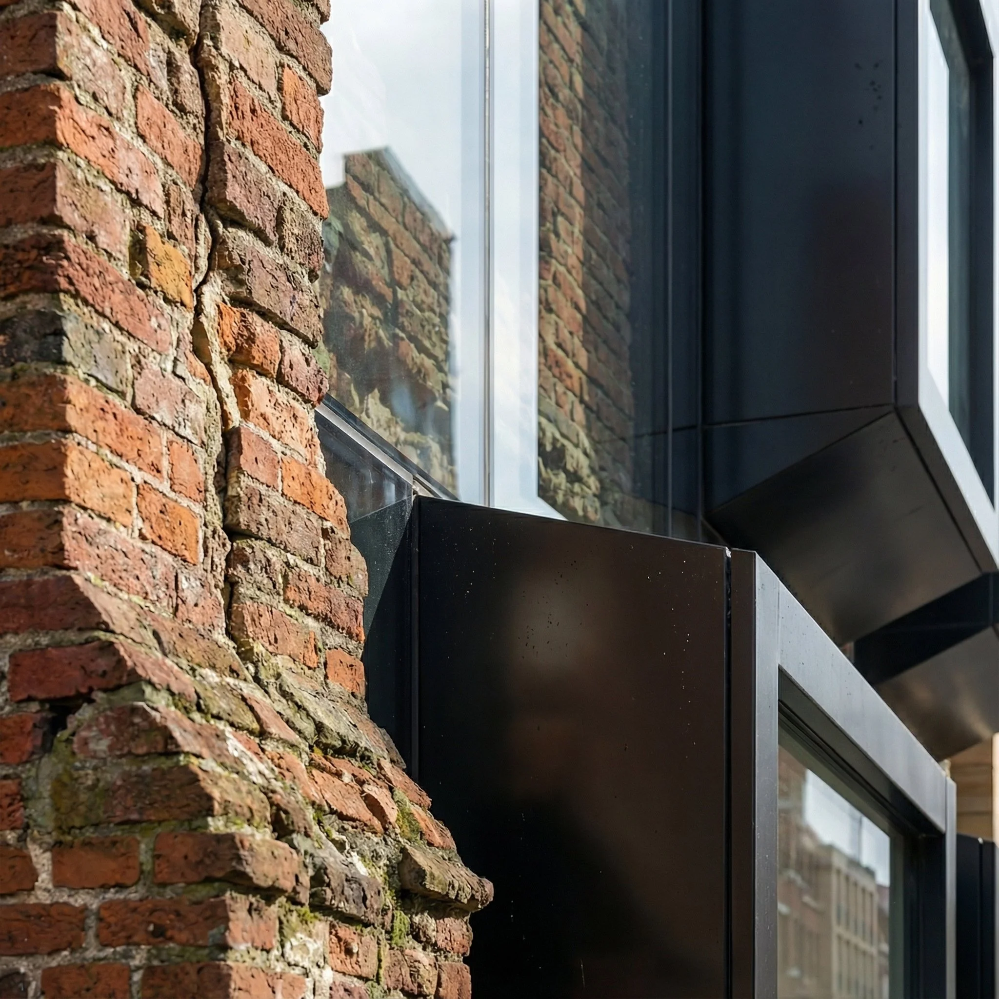 The contrast sharpens at the scale of detail. Dark, precise elements cut through the irregularity of the brick, establishing a clear distinction between past and present. Rather than blending, the two conditions define each other.