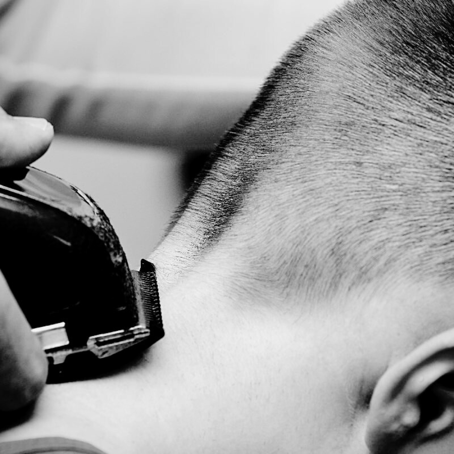 Une personne coupe les cheveux d'une autre personne avec des tondeuses, en noir et blanc.
