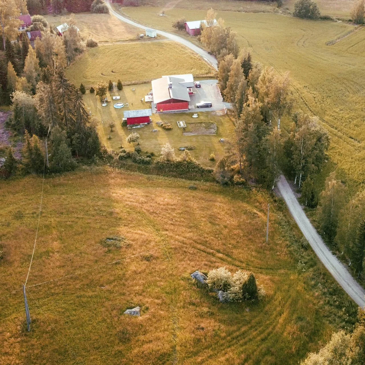 Ilmakuvassa näkee pienen maalaistalon pihapiirin ja ympäröivän maaseutualueen, sisältäen talon, piharakennuksia, puita, autoja ja tietä.