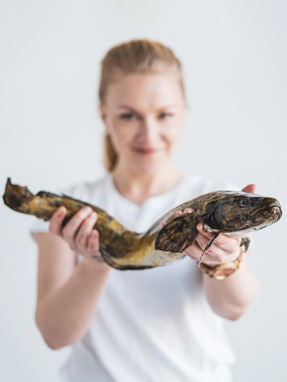 Nainen pitää kädessään suurta kalaa, taustalla valkoinen seinä.