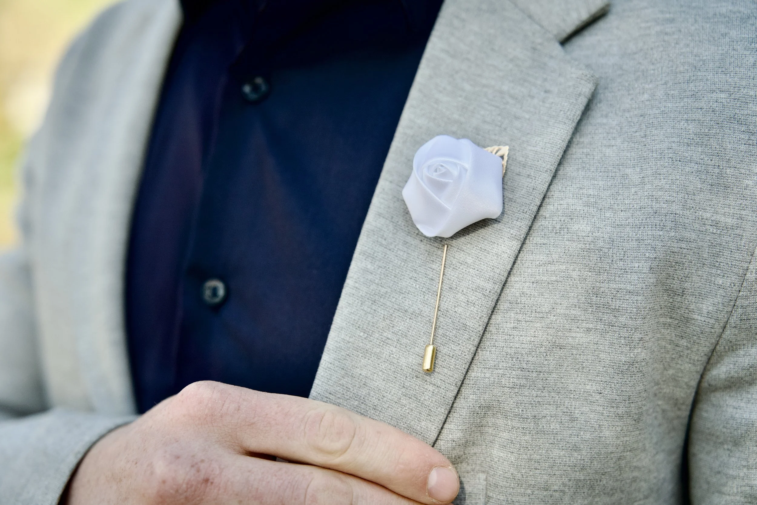 Férfi öltönyzakó közeli képe fehér virágos hajtókatűvel, bokrétával.