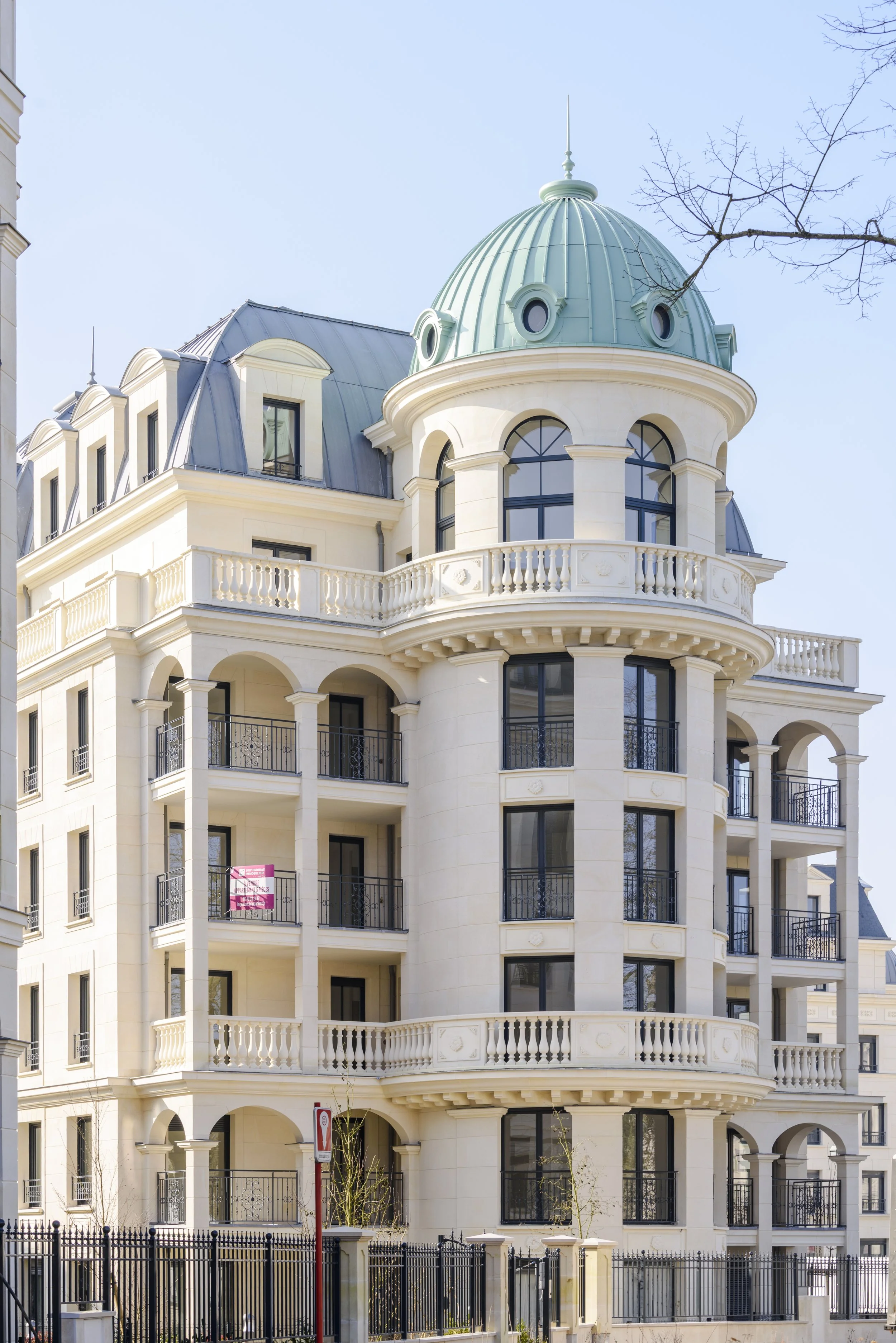 Bâtiment résidentiel élégant avec plusieurs étages, balcons en fer forgé, et un dôme vert en cuivre sur la tour principale, dans un style architectural néoclassique.