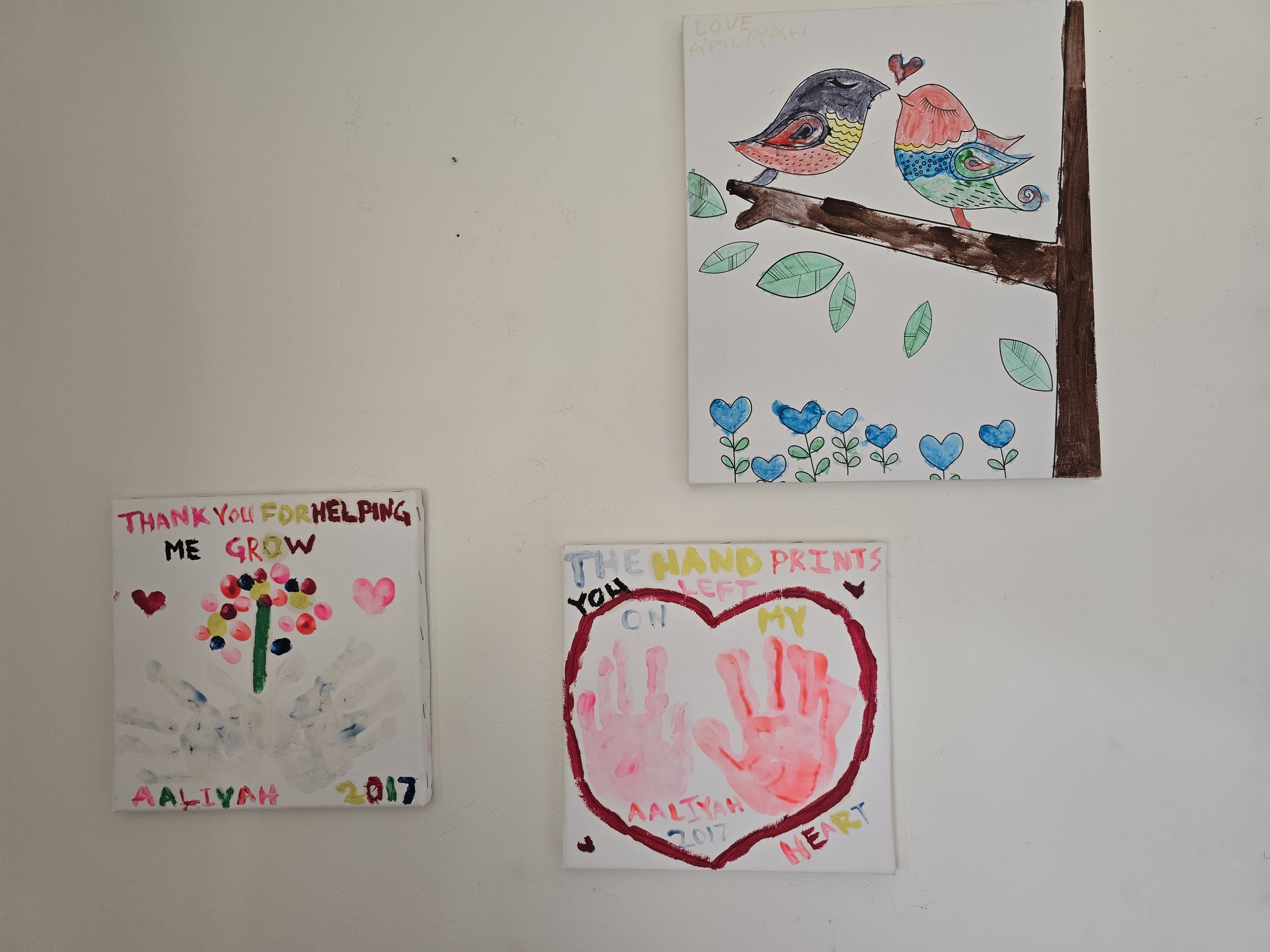 Three children's drawings on paper and a colored drawing of two birds on a tree branch.