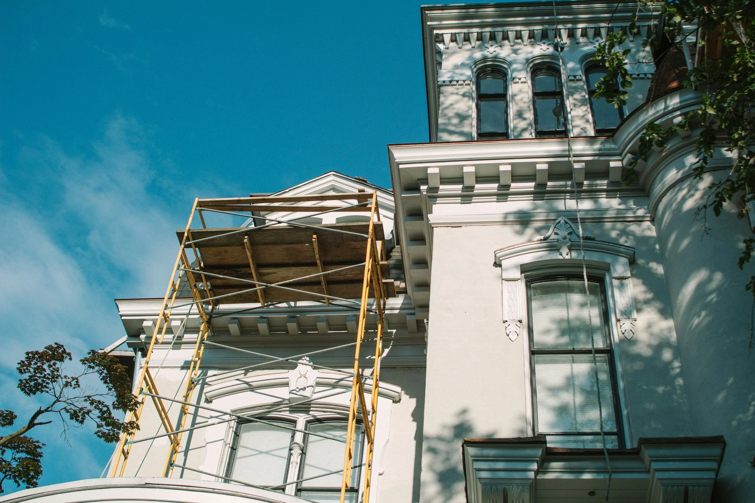 Et hvitt hus med arkitektoniske detaljer og store vinduer, delvis dekket av en sklie av stigerør, under en klar blå himmel.