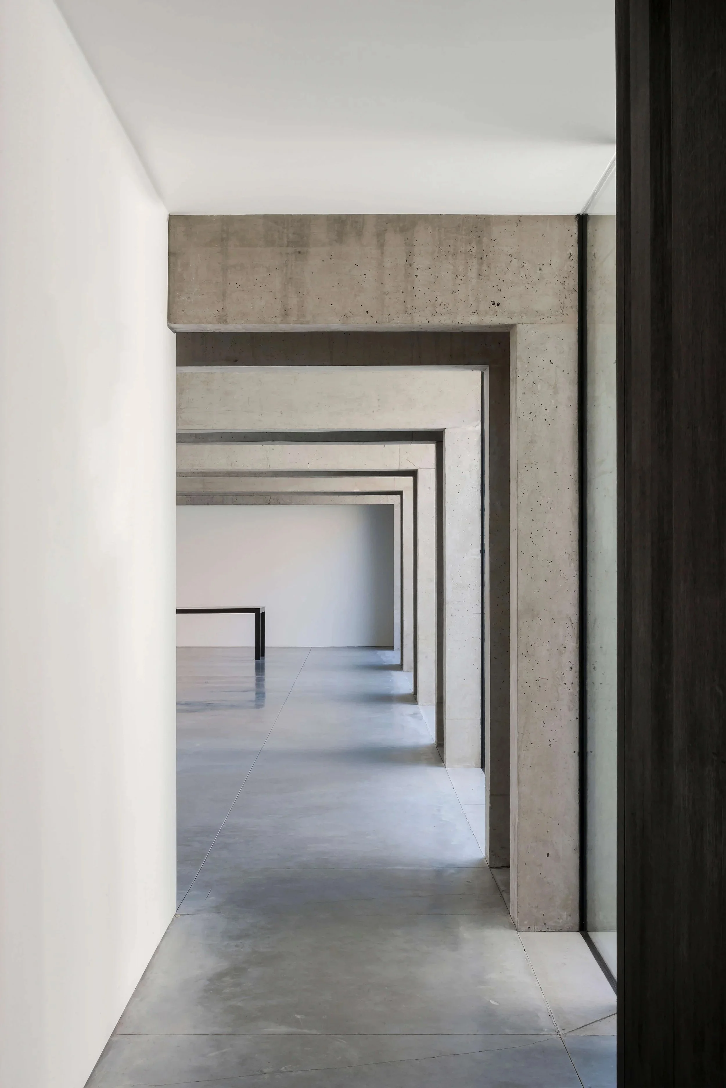 En lang gang med flere dører, vegger og tak laget av betong, med minimalistisk og moderne arkitektur.