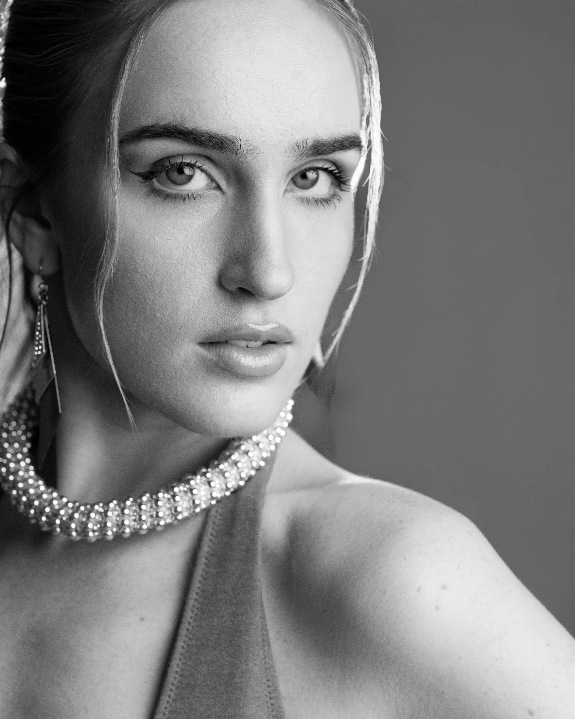 Kyra, close-up black and white portrait with direct gaze, crystal choker necklace, bare shoulder, studio