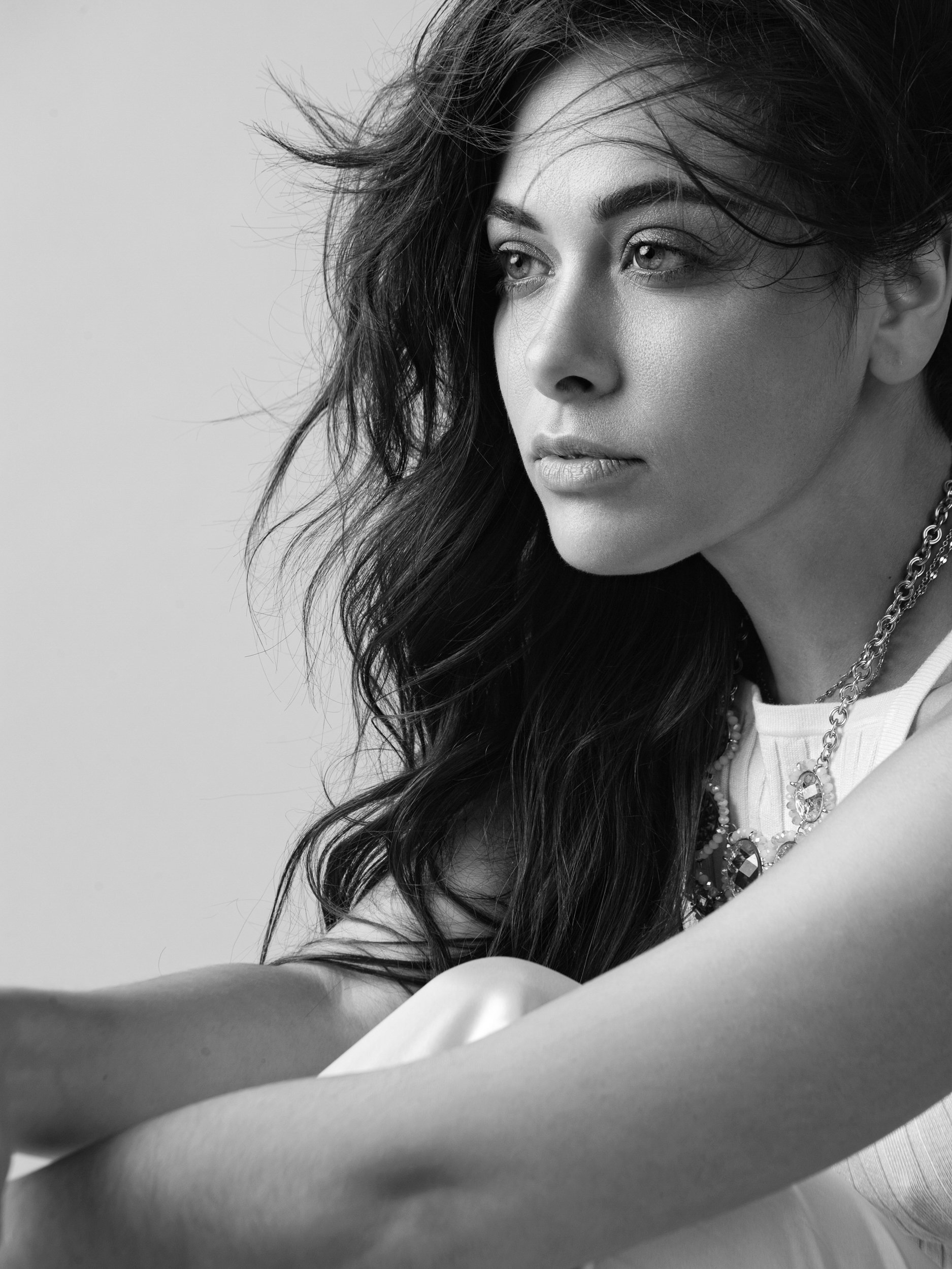 Nina, black and white portrait with off-camera gaze, windswept dark hair, statement chain necklace, studio