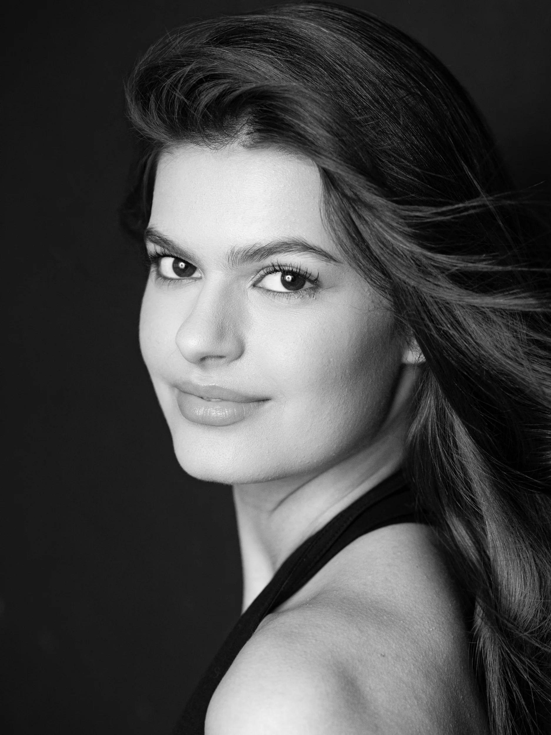 Elisa, black and white portrait looking back over shoulder with composed gaze, long dark hair, bare shoulder, studio