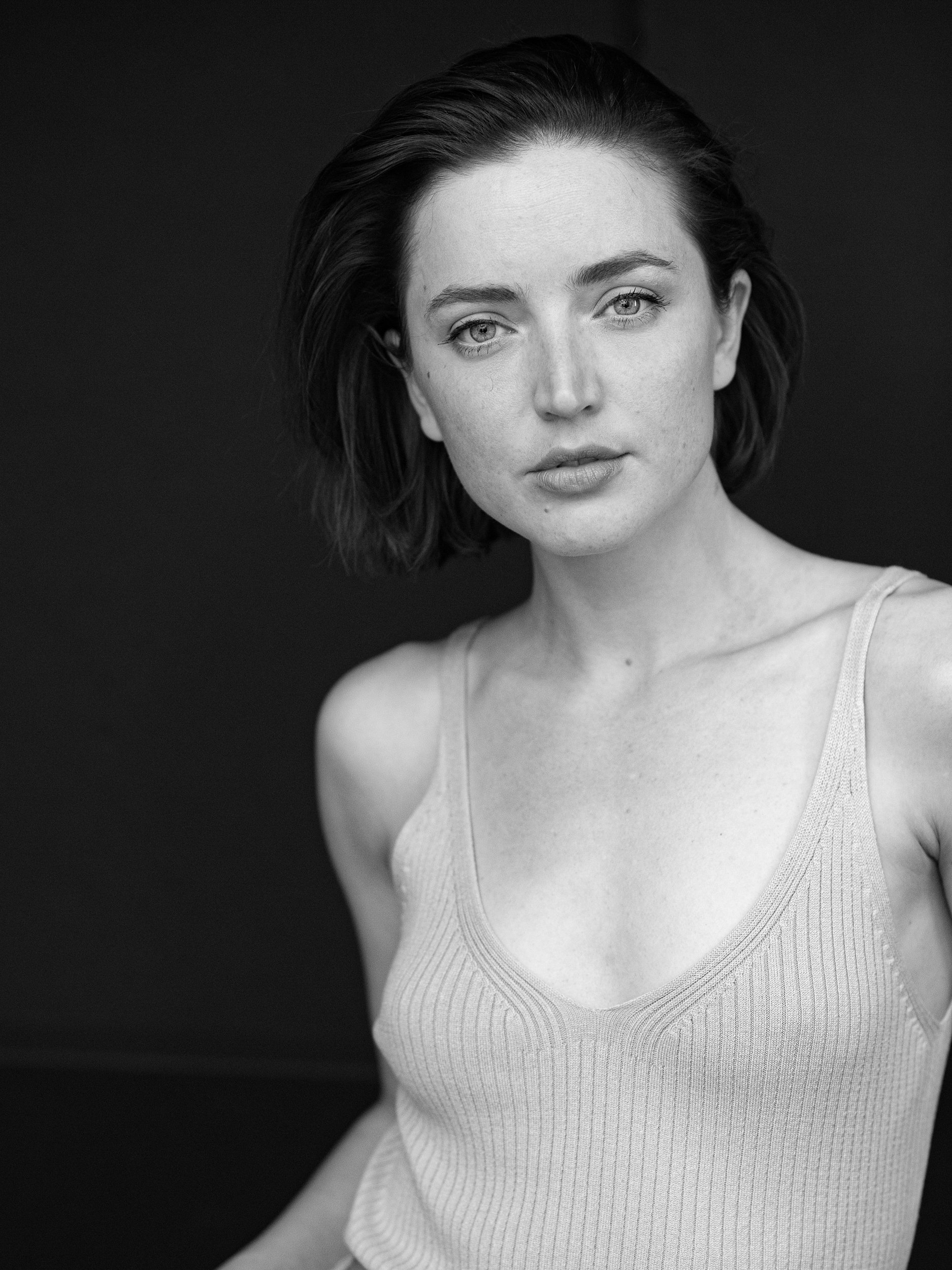 Annalise, black and white close-up portrait with direct gaze, short dark bob, freckles, ribbed knit top, dark studio background