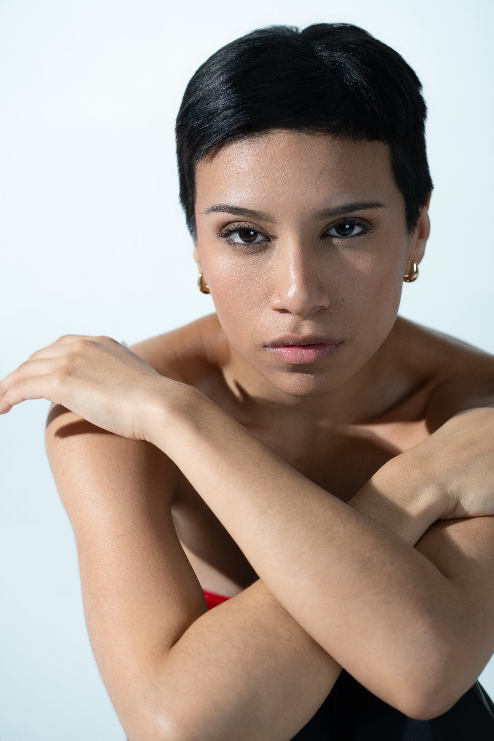 Amanda, portrait session at 9 Studios, SoHo NYC — close editorial portrait, arms crossed at chest, direct gaze, gold hoop earrings, bright white background, May 2026